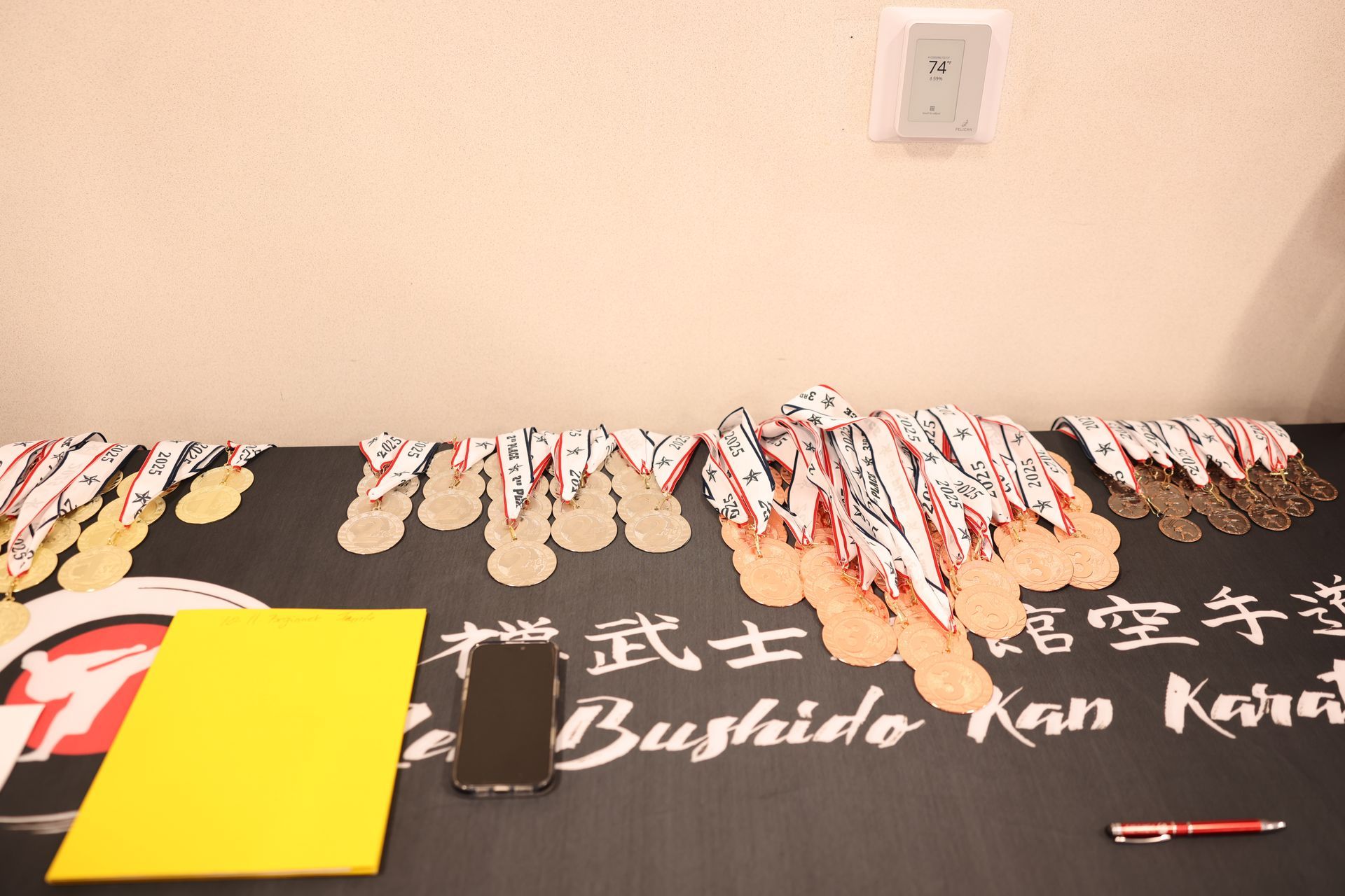 Karate tournament table with medals, certificates, a phone, and pen.