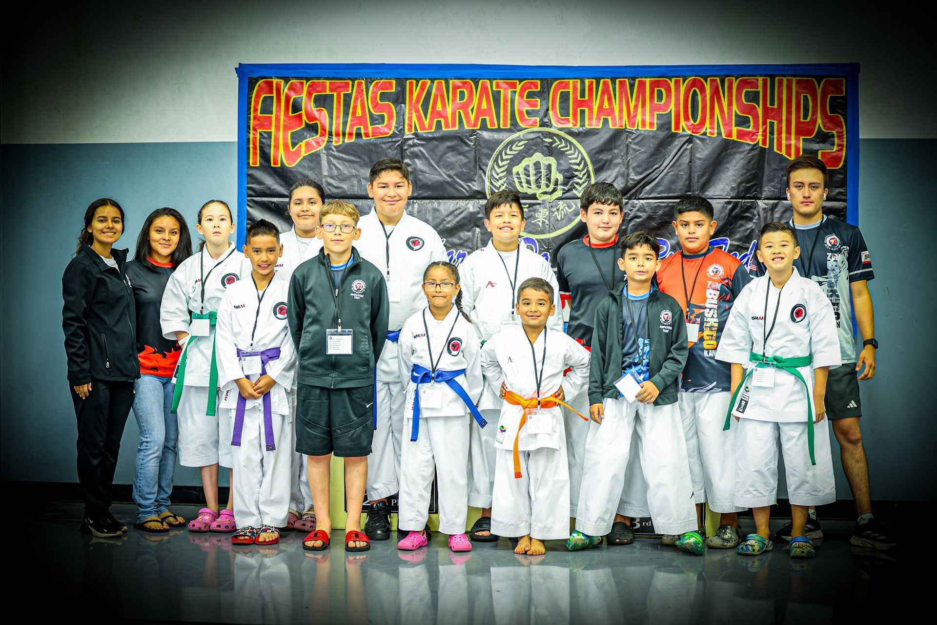 Karate tournament group photo with athletes and coaches. Children in white uniforms, banner 