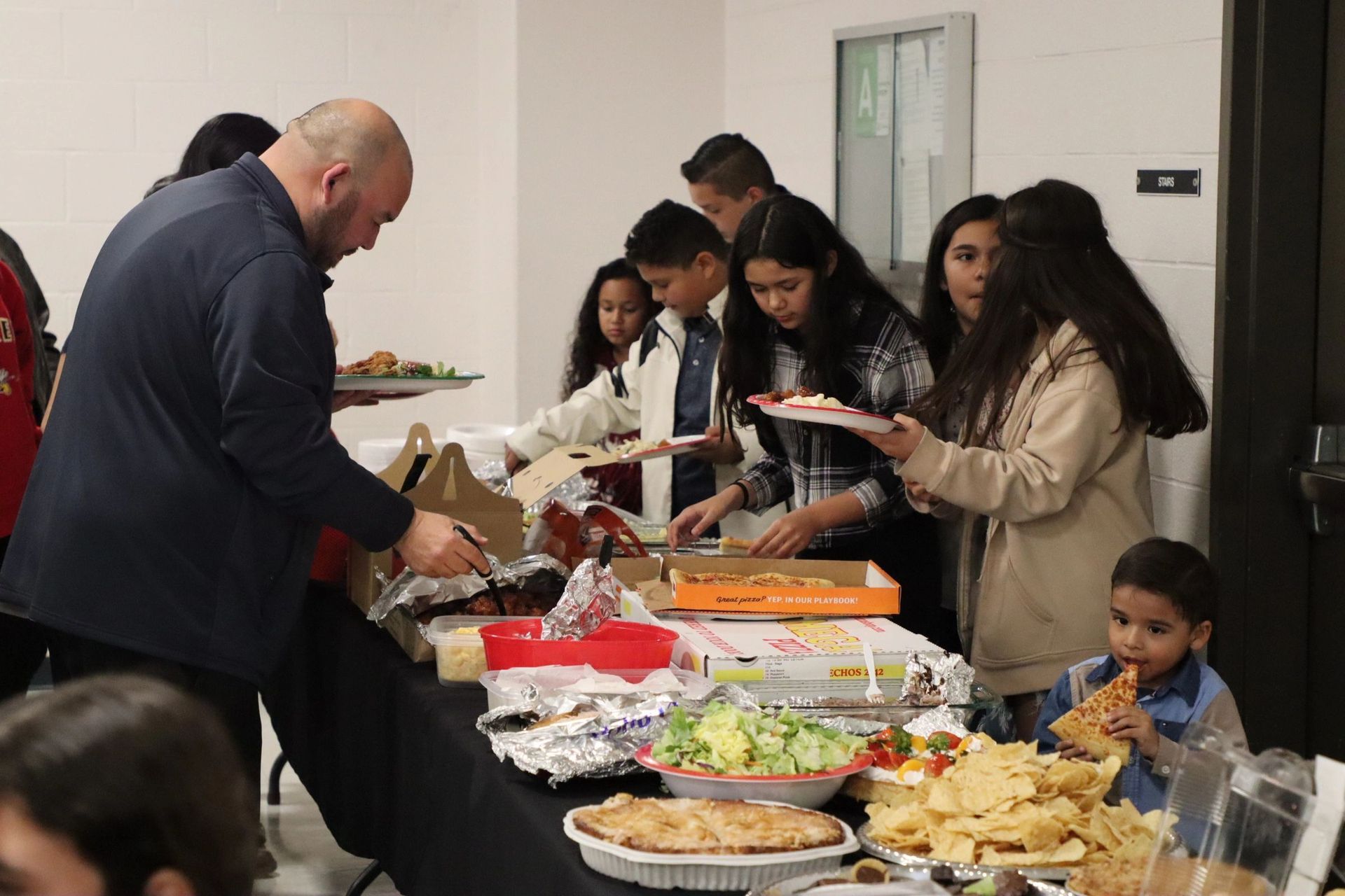 A group of people are standing around a table eating food.