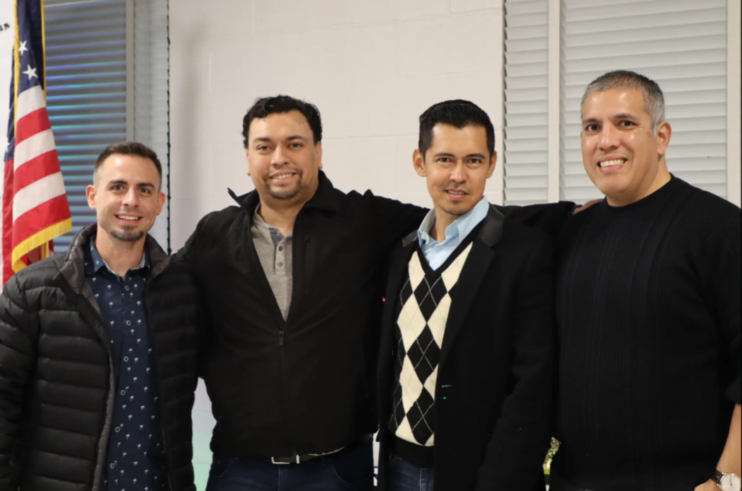 Four men are posing for a picture in front of an american flag.
