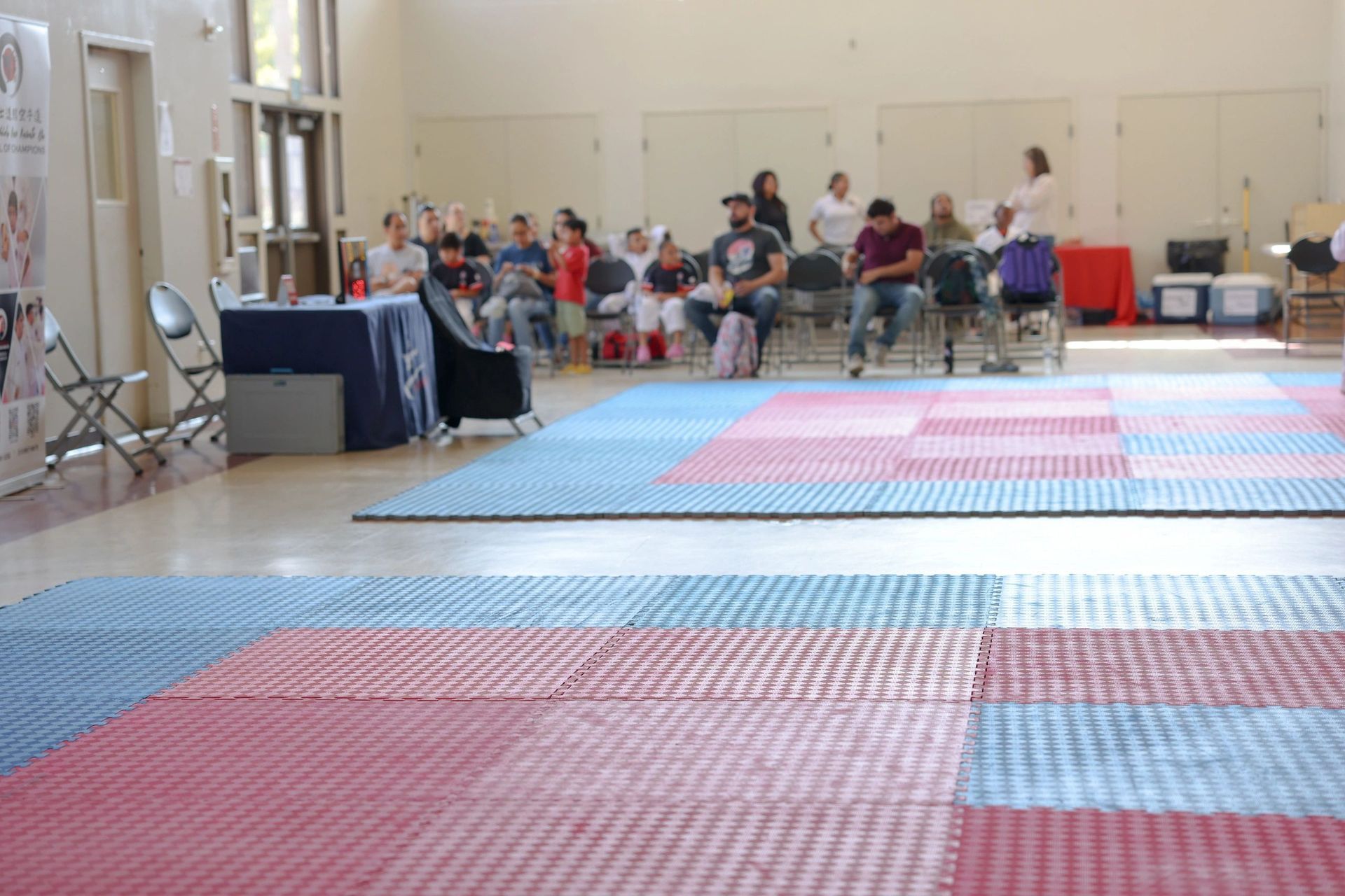 A group of people are sitting in chairs in a room with red and blue mats on the floor.