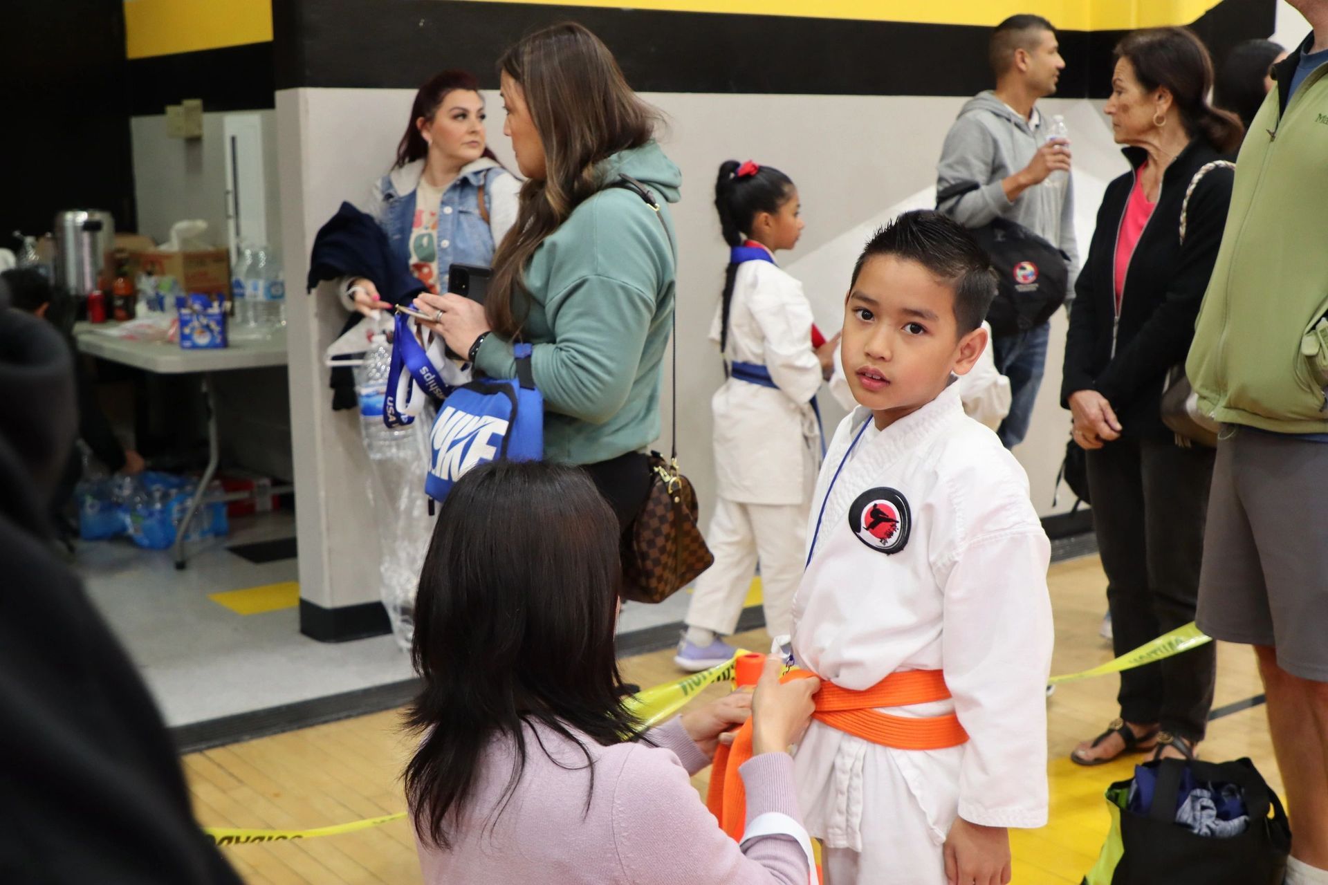 A woman is helping a young boy with his karate uniform.