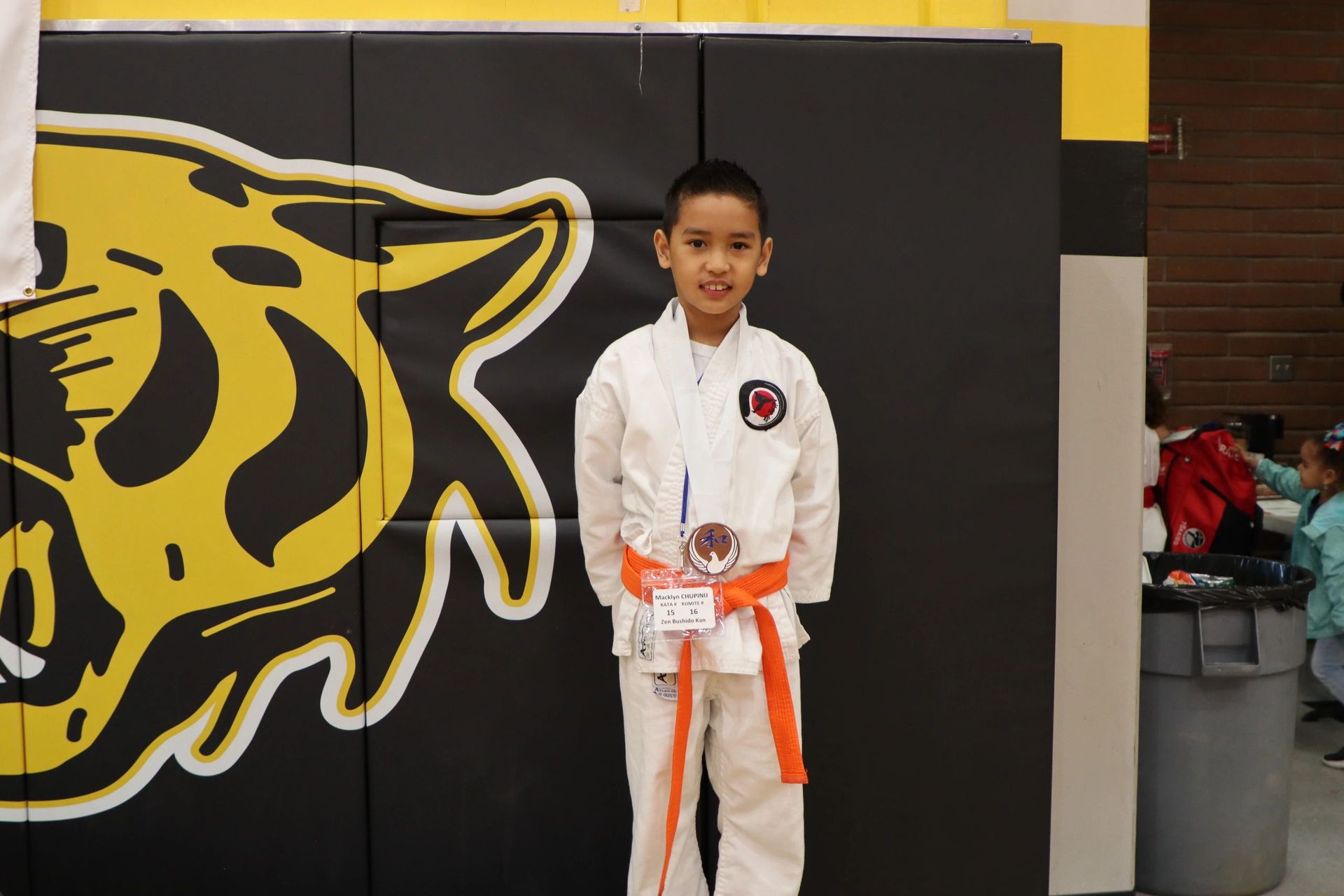 A young boy in a karate uniform is standing in front of a wall with a tiger on it.