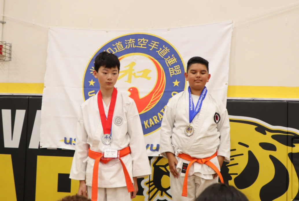Two boys are standing in front of a karate banner