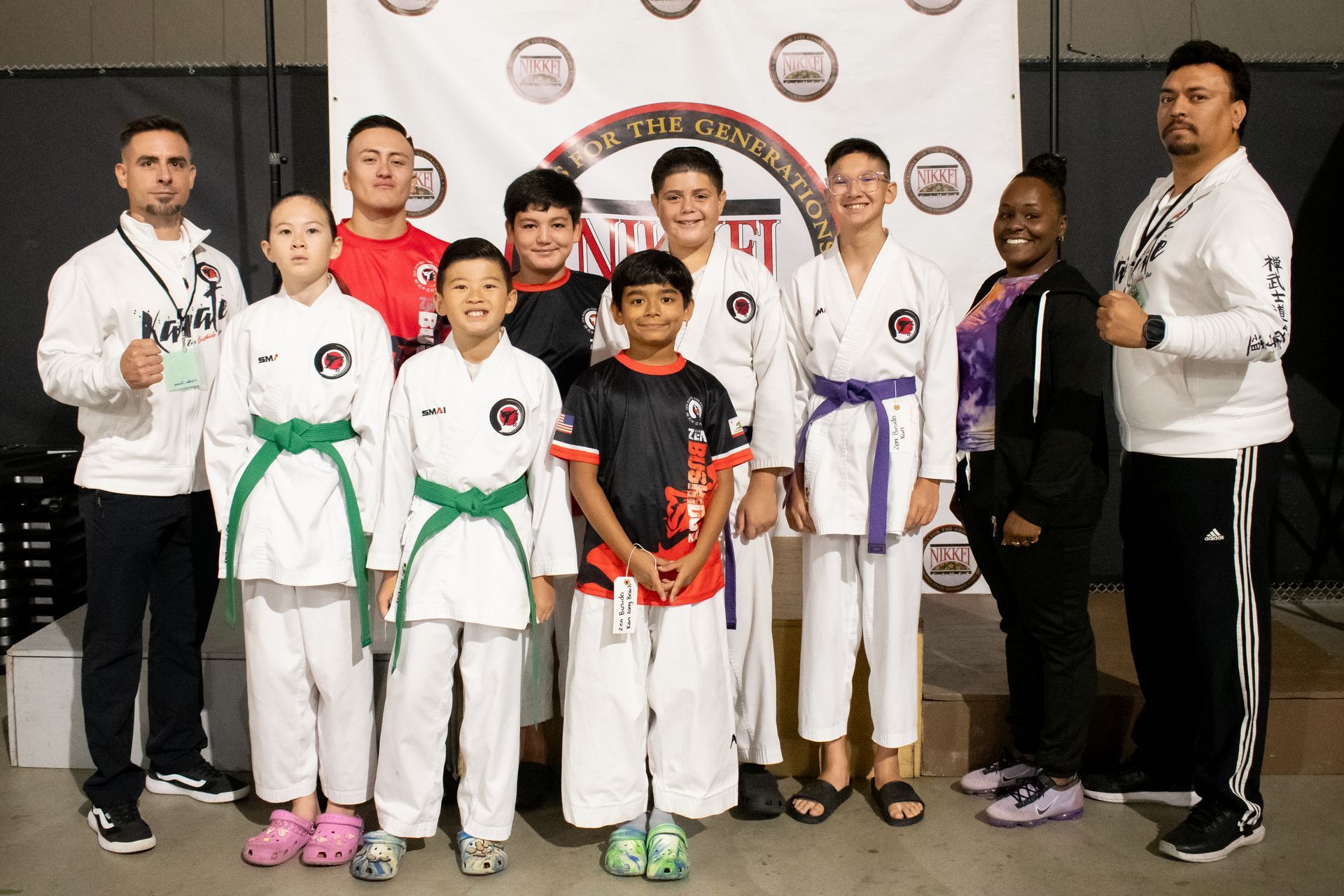 Group of karate students and instructors posing for a photo, wearing karate uniforms, black and red belts.