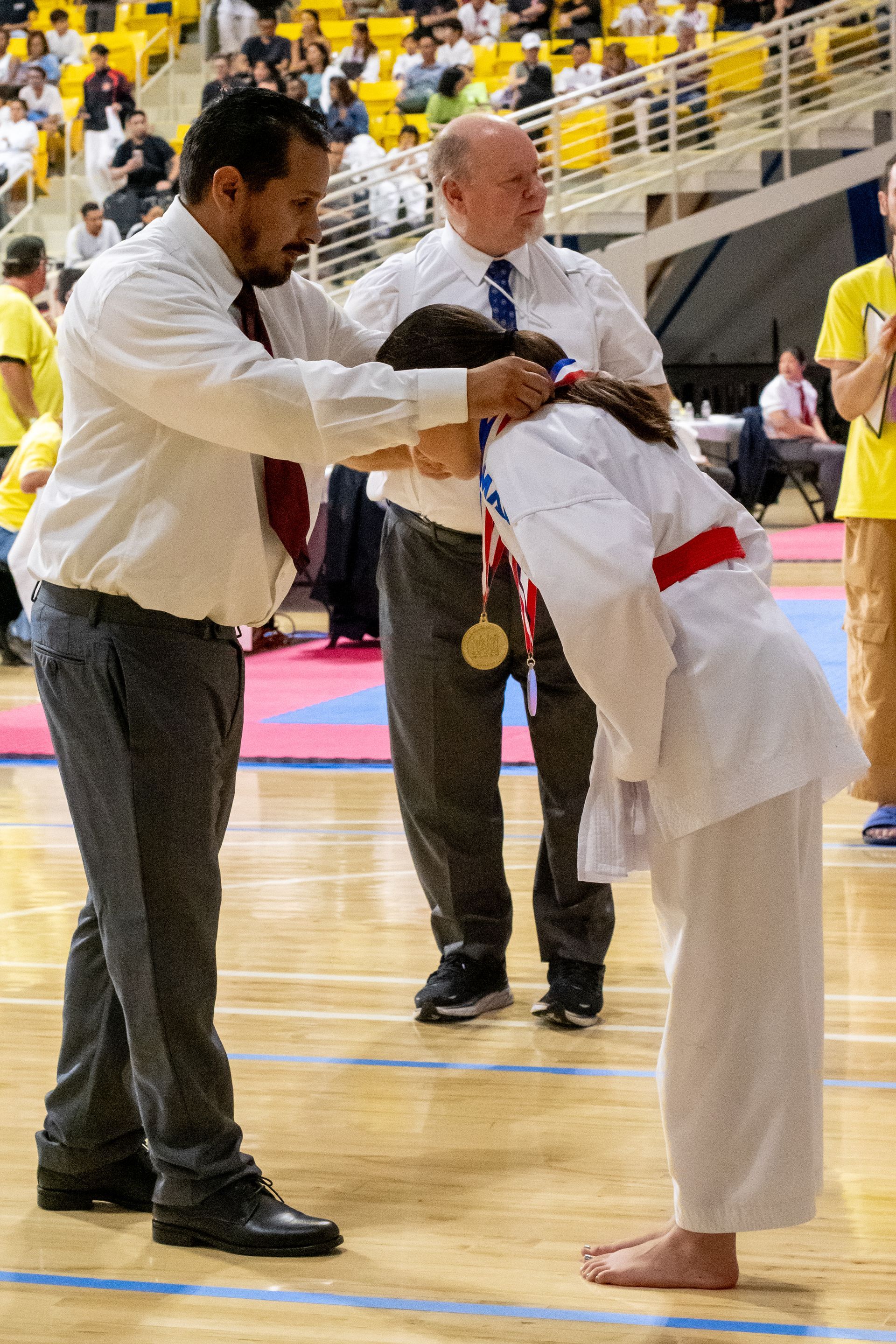 Man placing a gold medal on a bowing karate athlete at a tournament.