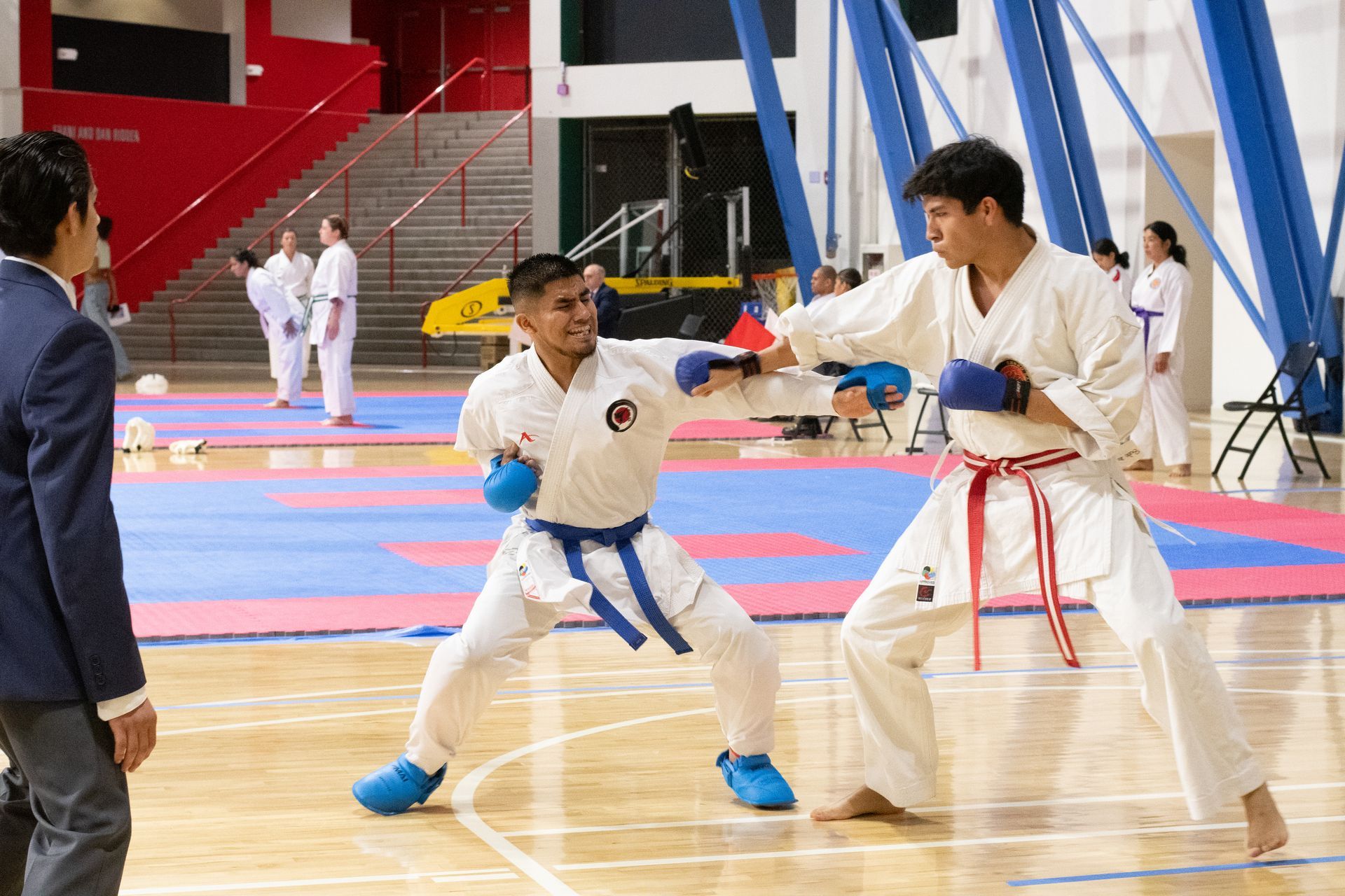 Two karate athletes in a match, one punches, the other blocks, in a gymnasium.