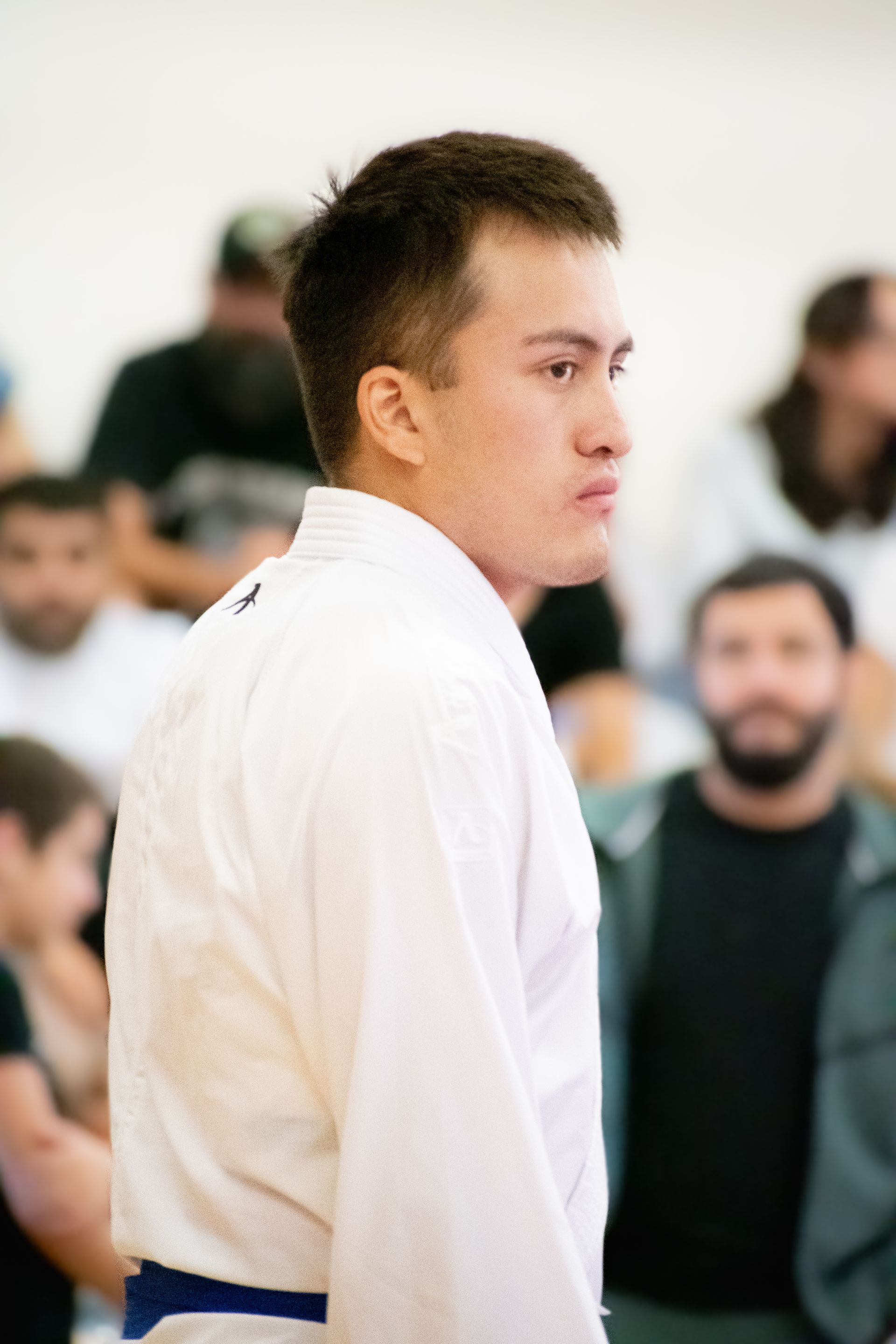 A young man in a white karate uniform is standing in front of a crowd.