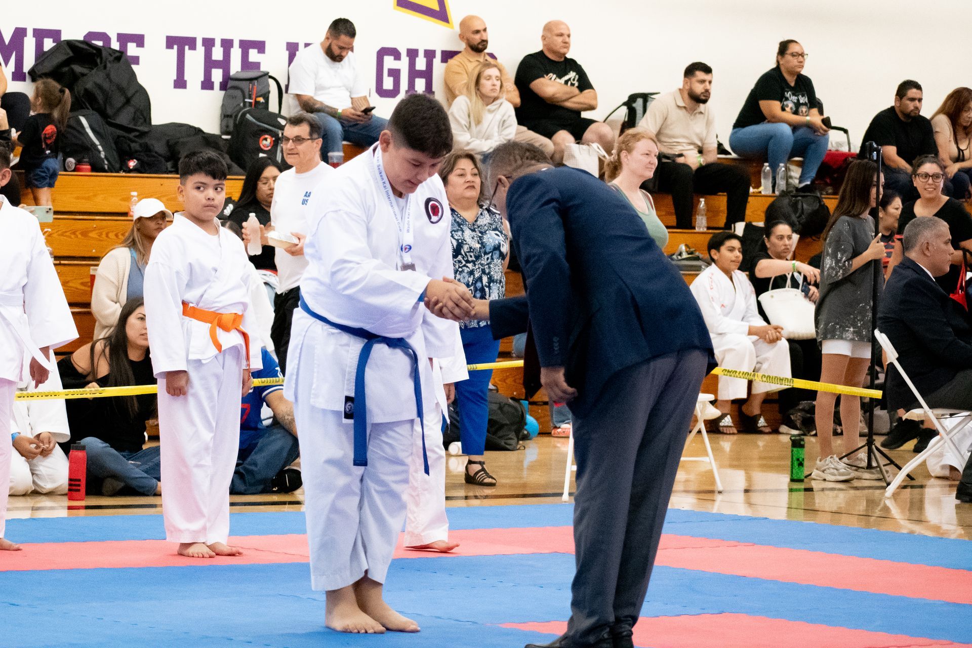 A man in a suit is kneeling down next to a boy in a karate uniform.
