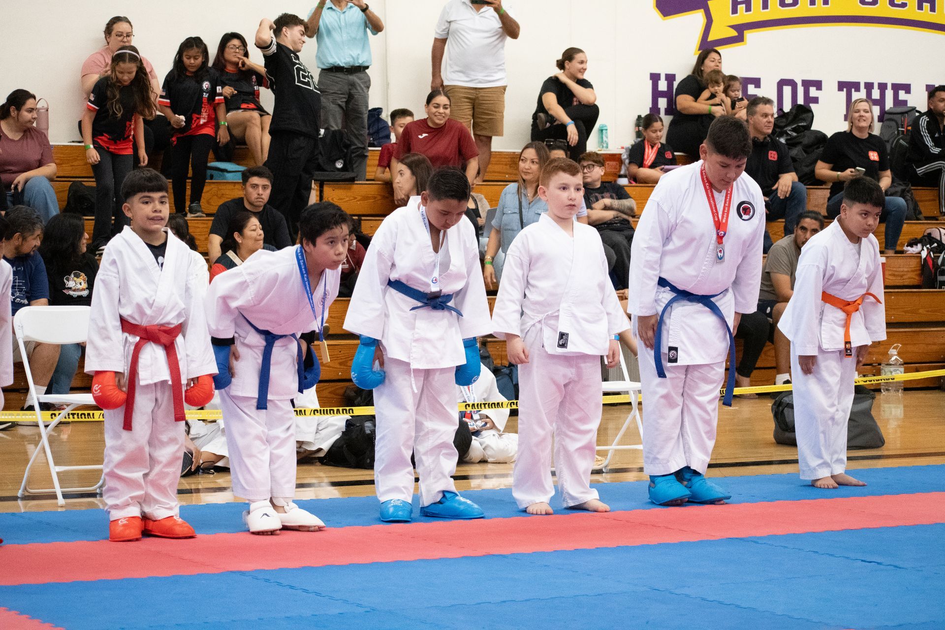 A group of young boys in karate uniforms are standing on a mat in a gym.