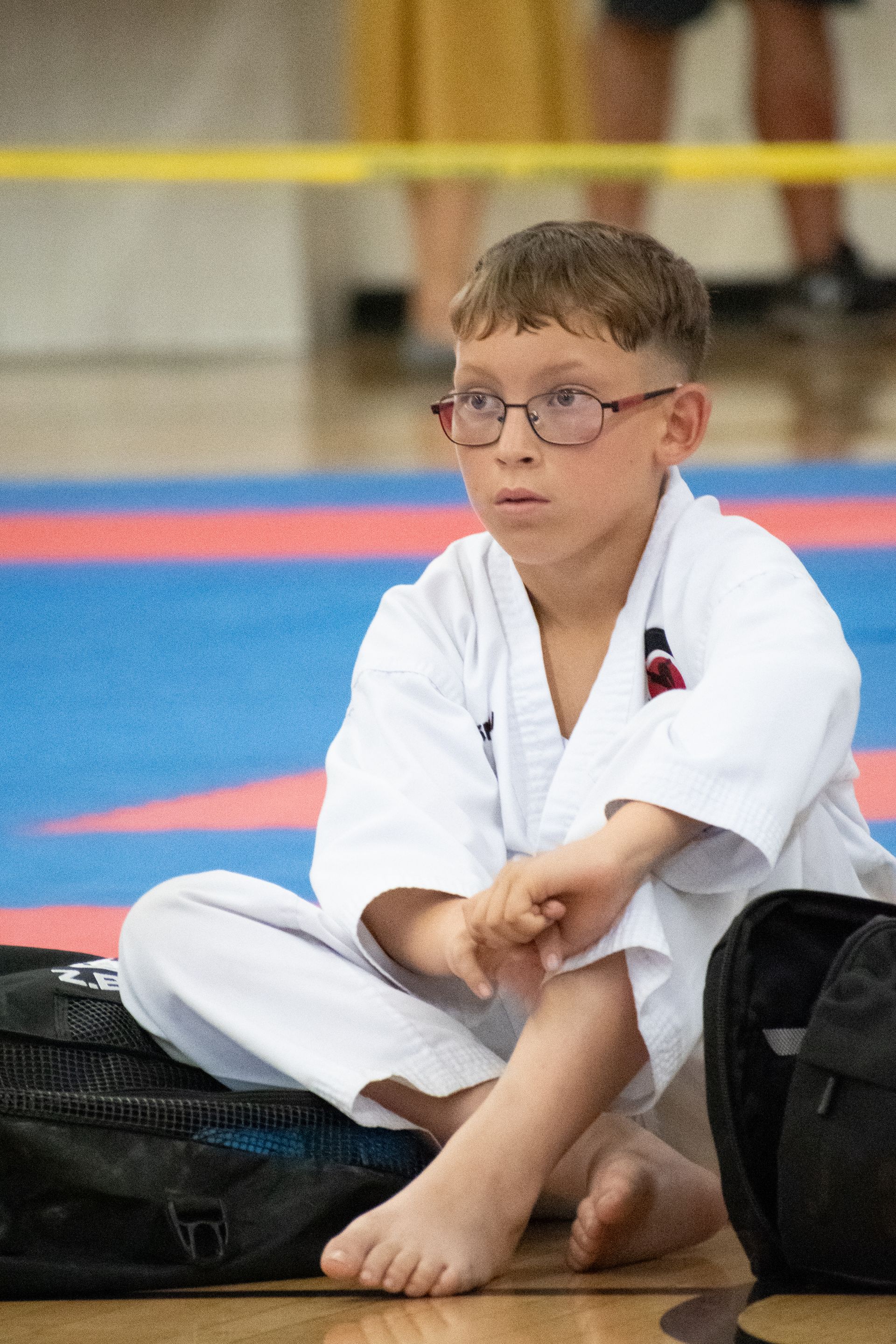A young boy in a karate uniform is sitting on the floor