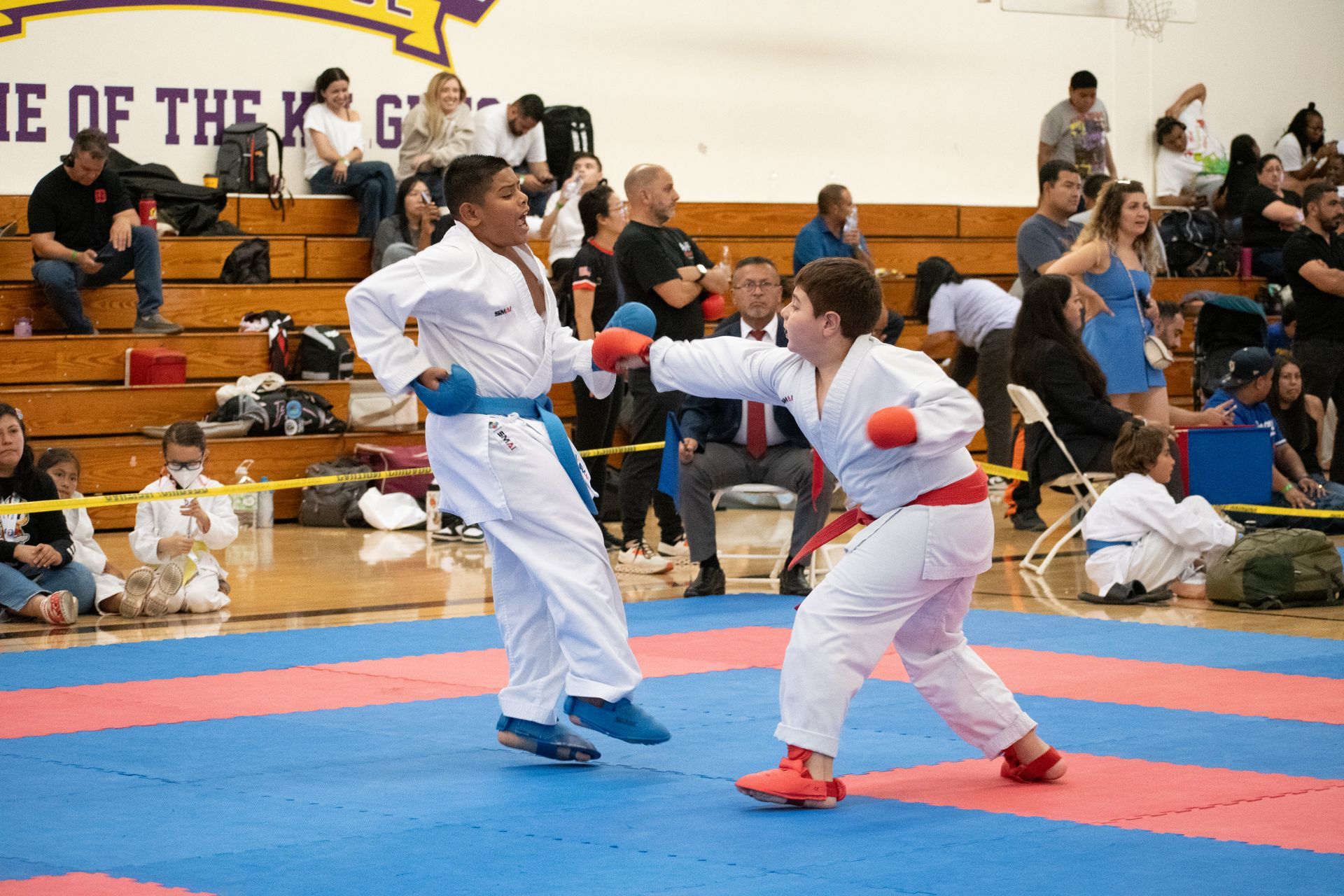 Two karate fighters are fighting on a mat in a gym.