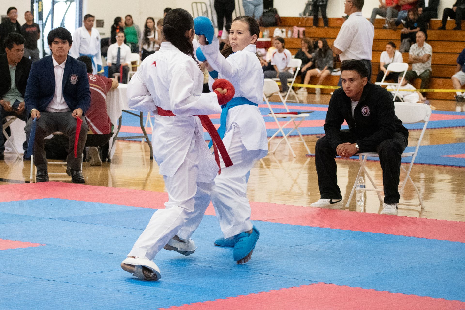 Two karate fighters are fighting on a mat with a referee watching