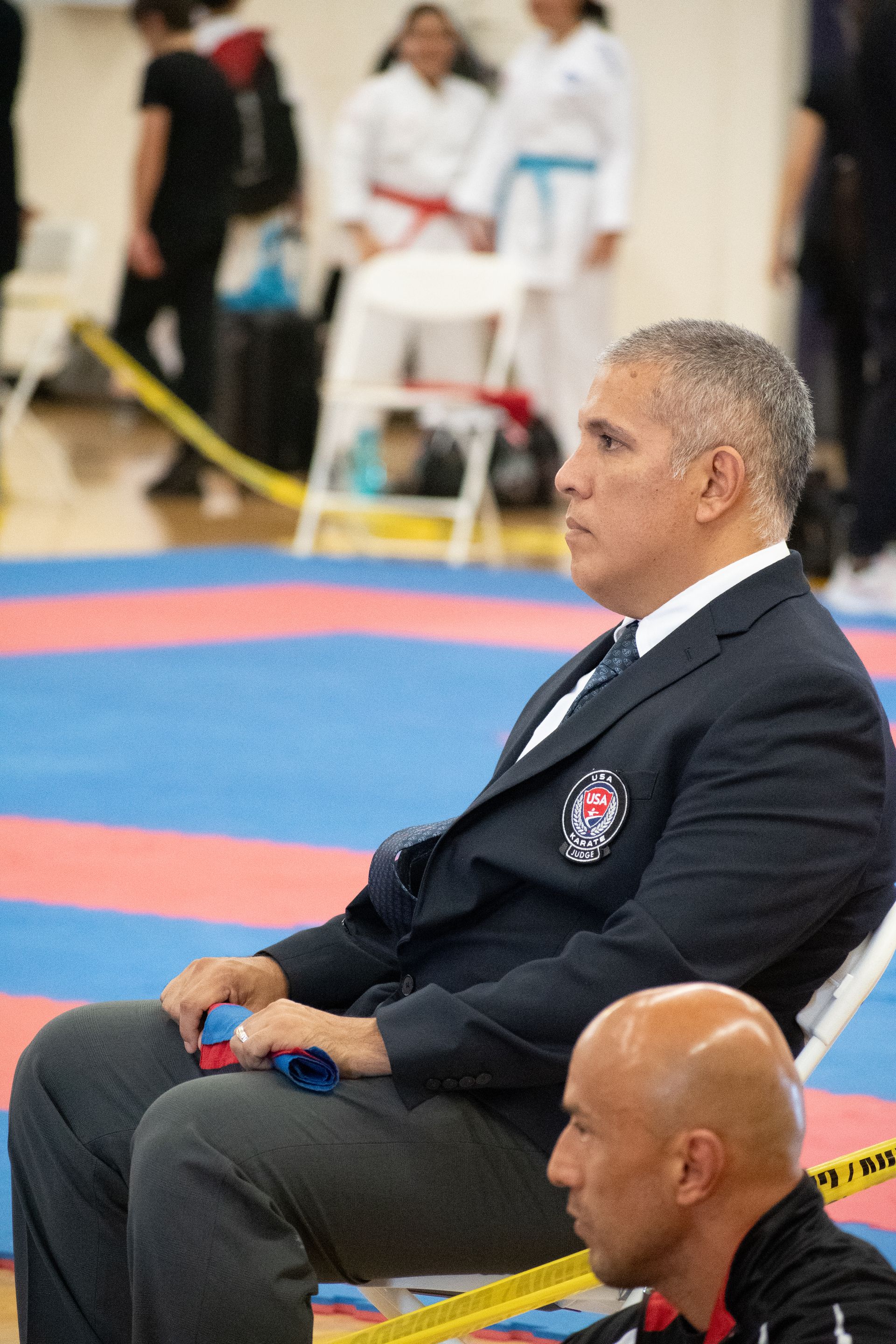 A man in a suit is sitting in a chair watching a karate match.