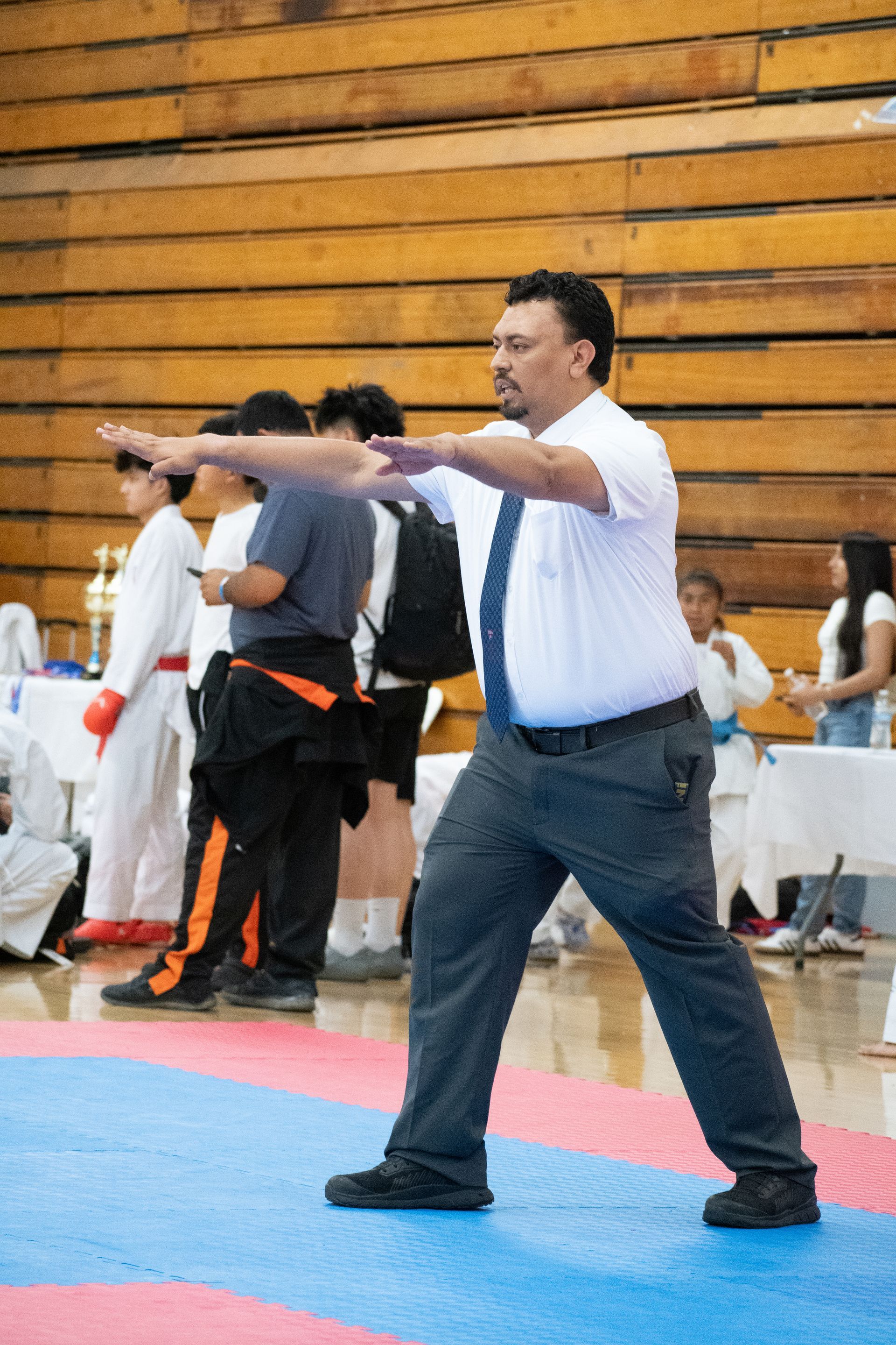 A man in a white shirt and tie is standing on a karate mat.