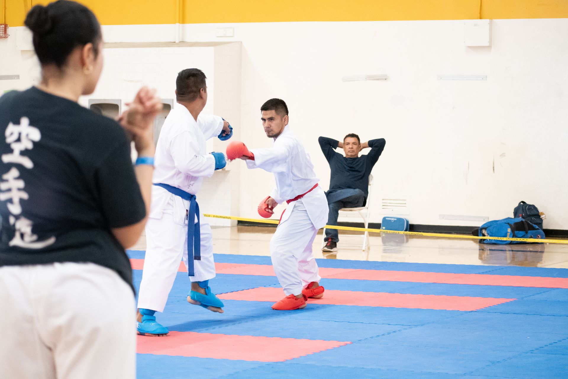 A man is sitting on a bench watching two karate fighters