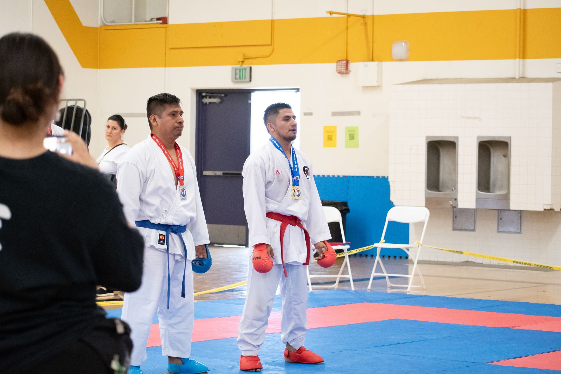 Two men in karate uniforms are standing on a mat in a gym.