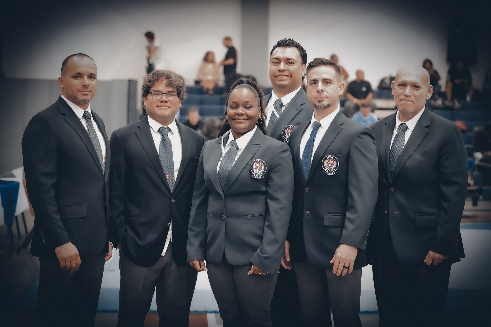 Group of six people in dark suits posing indoors,  at a competition.