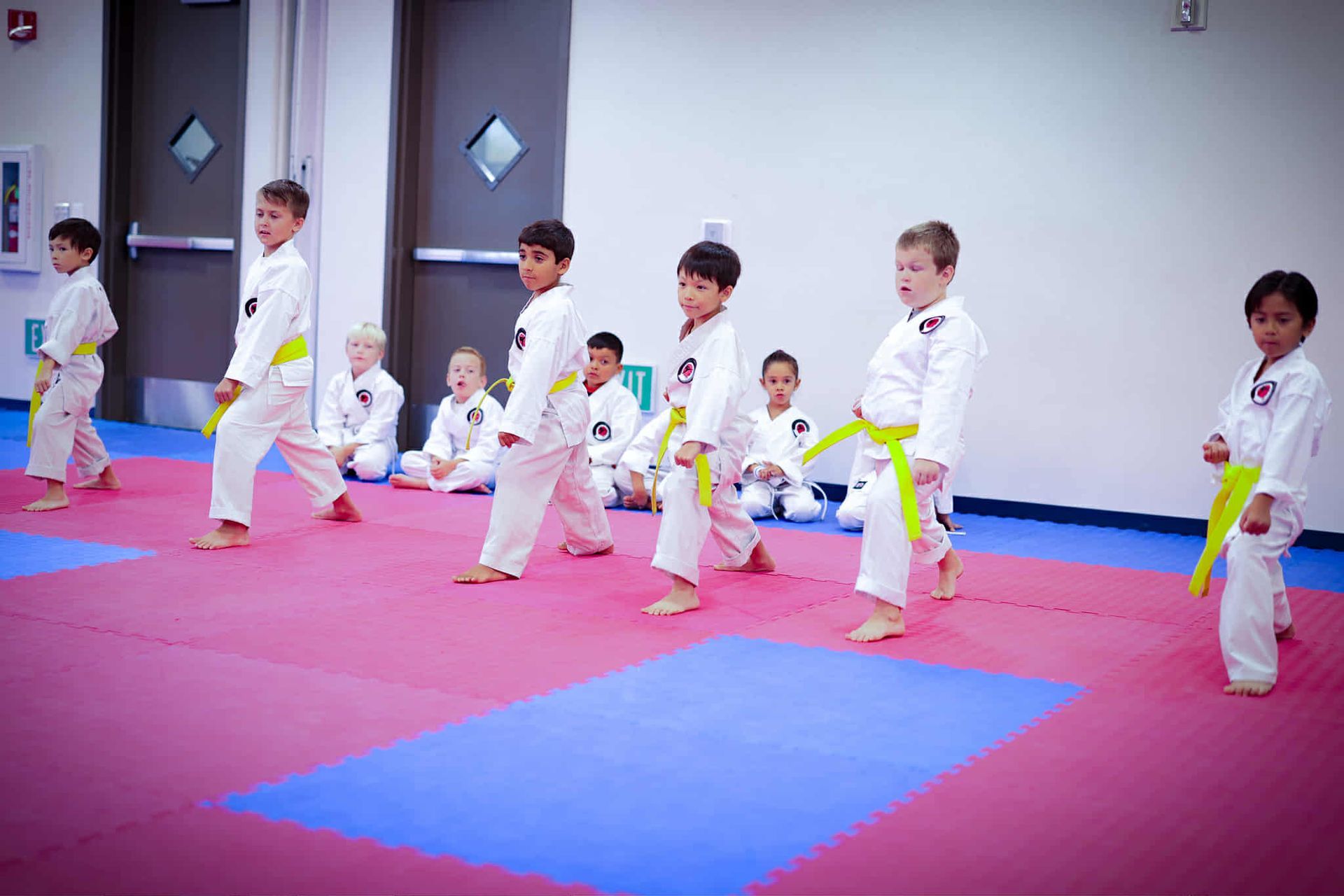 Children in white martial arts uniforms practice karate on colorful mats.