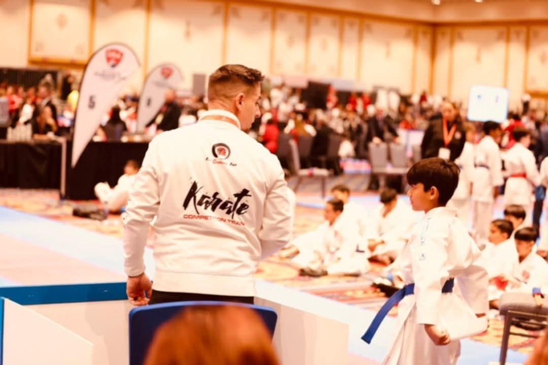 A man in a karate uniform is standing in front of a group of children.