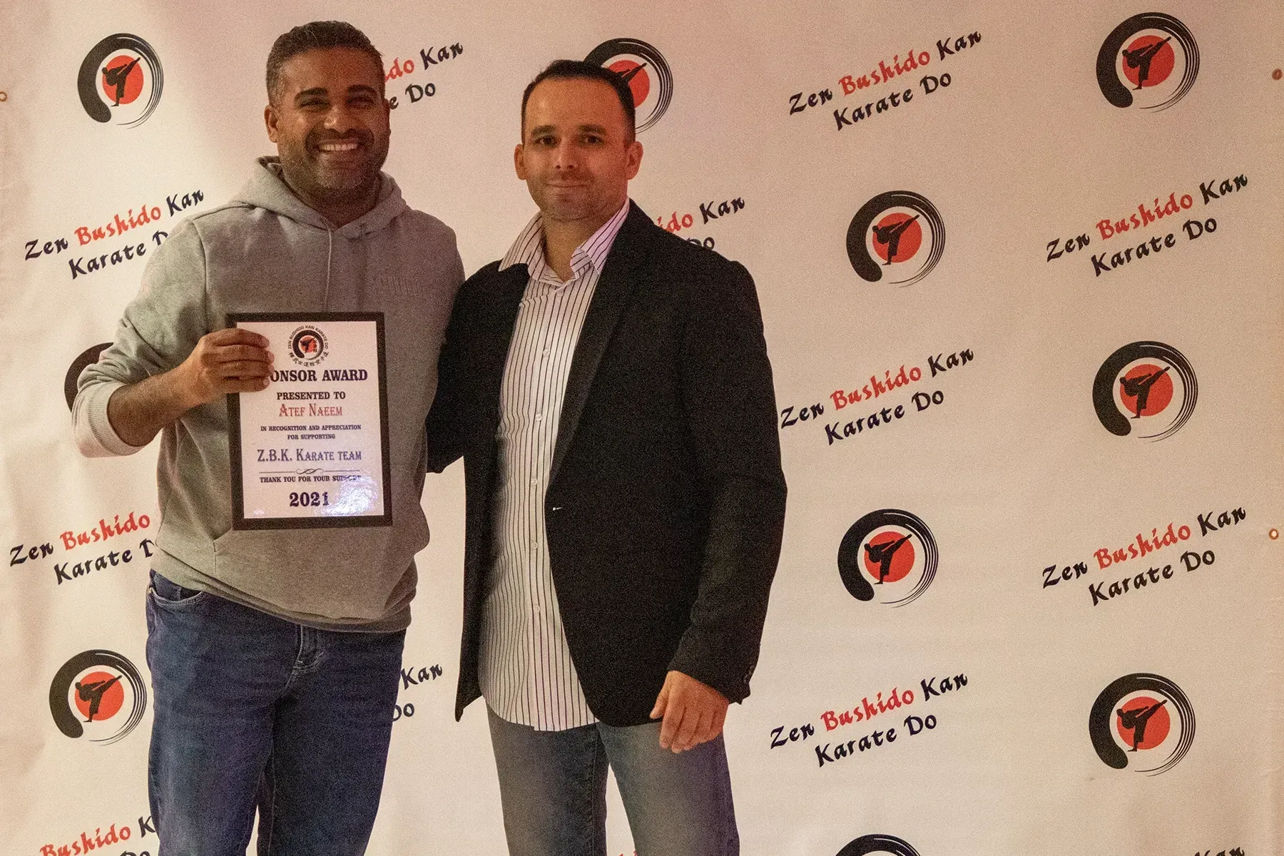 Two men are standing in front of a wall that says zen bushido karate do