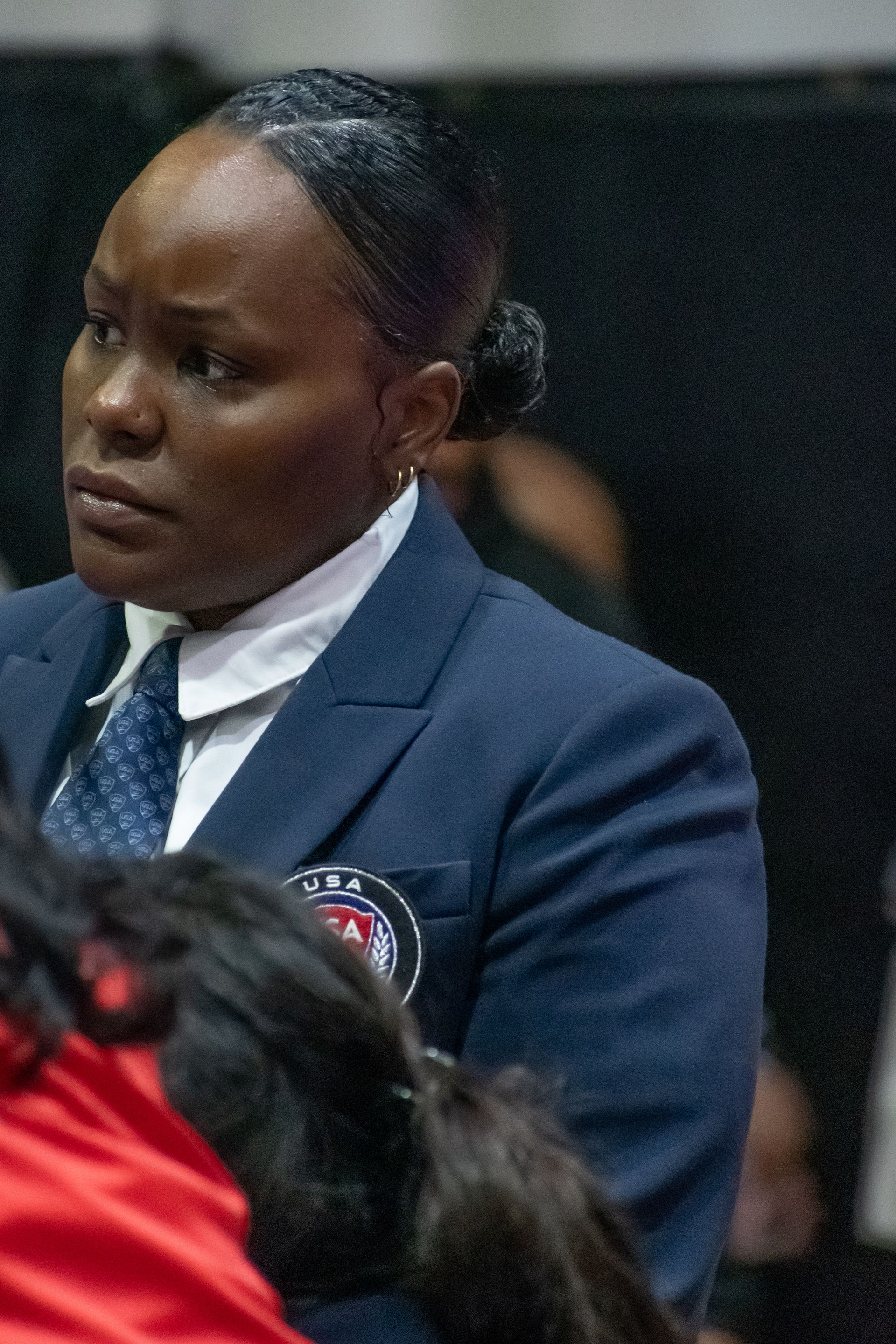 Woman in a blue suit, white shirt, and tie; looking to the side, focused.