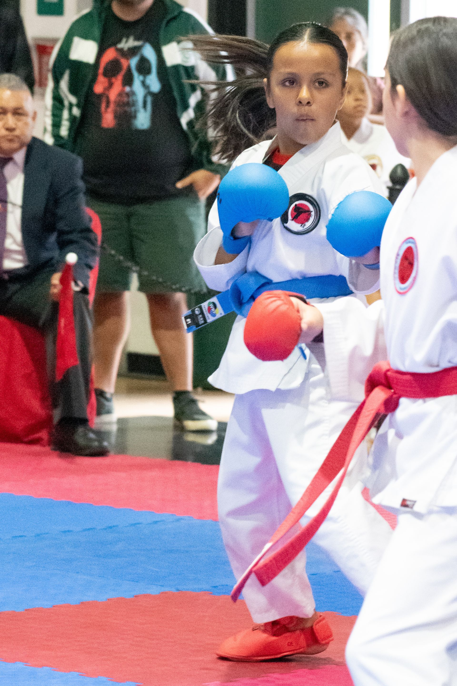 Young karateka in white uniform and blue gloves facing opponent in red.