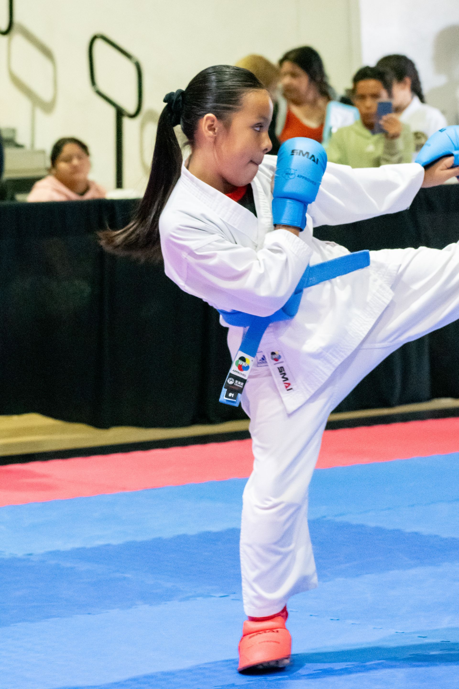 Young person in karate uniform kicking, blue belt, in a competition.