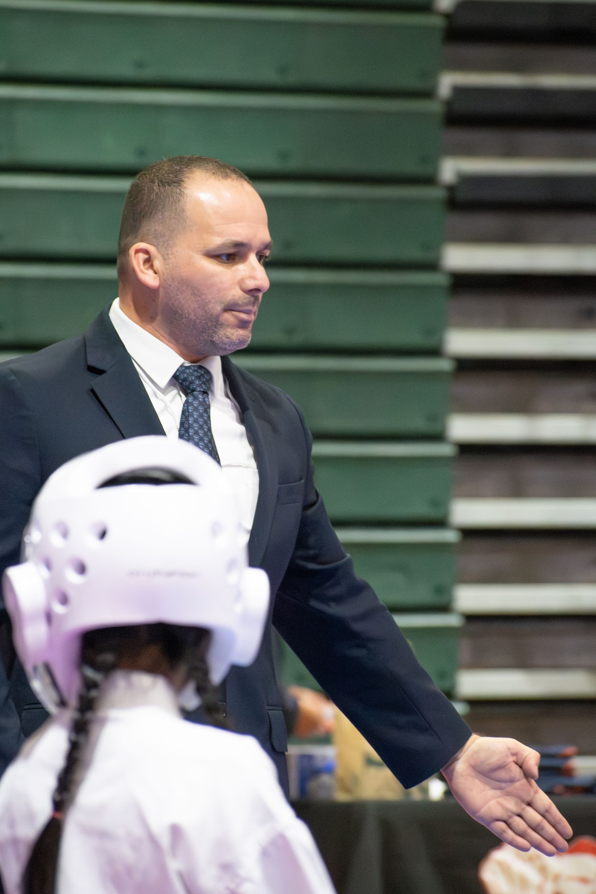 Man in suit coaching child in karate uniform at competition.