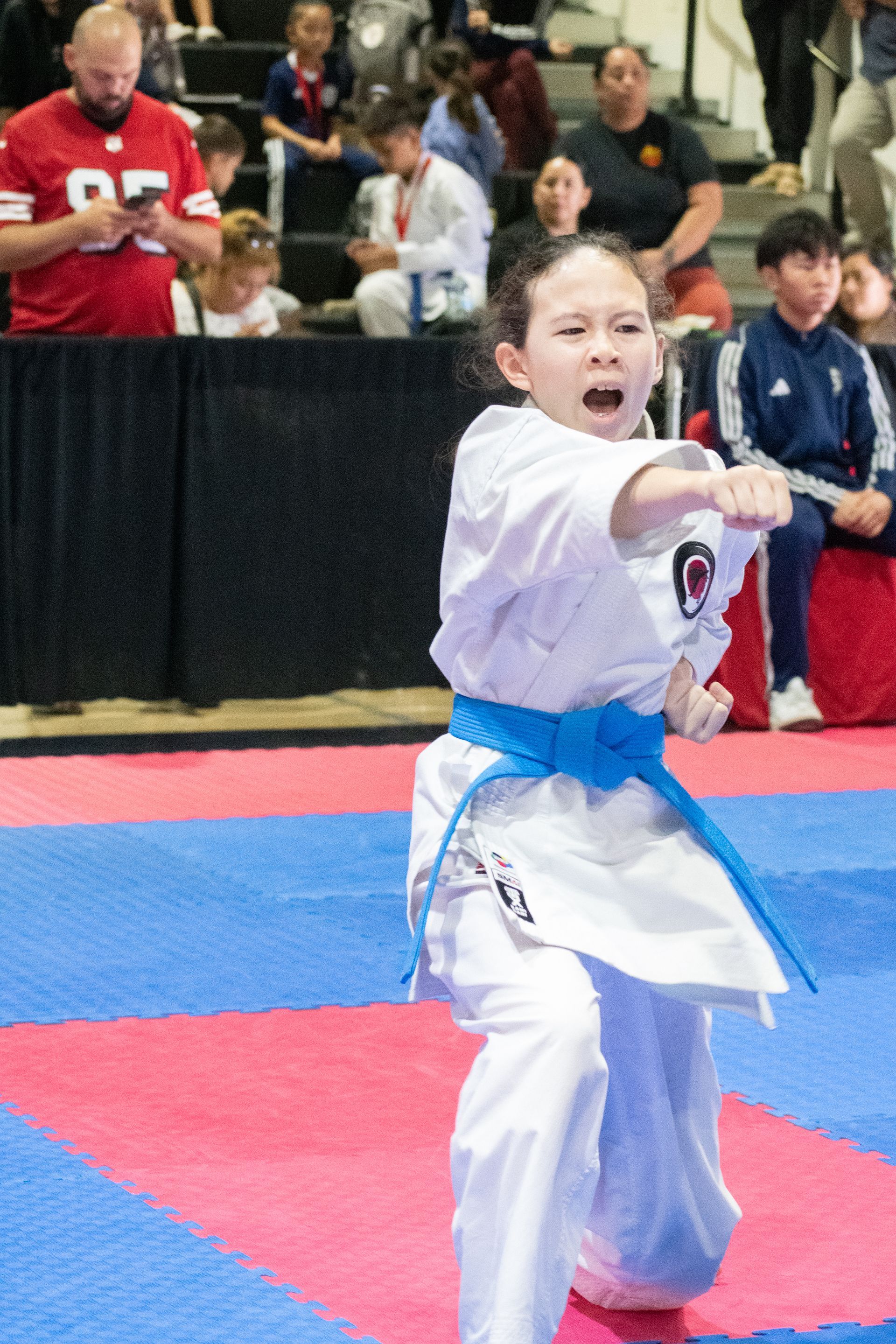 Young karateka in white uniform and blue belt performing a punch during a competition.