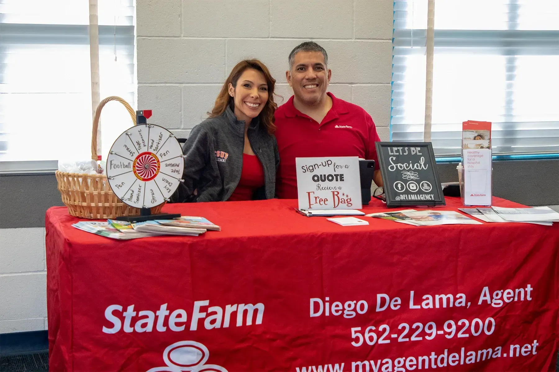 A man and a woman are standing behind a state farm table.