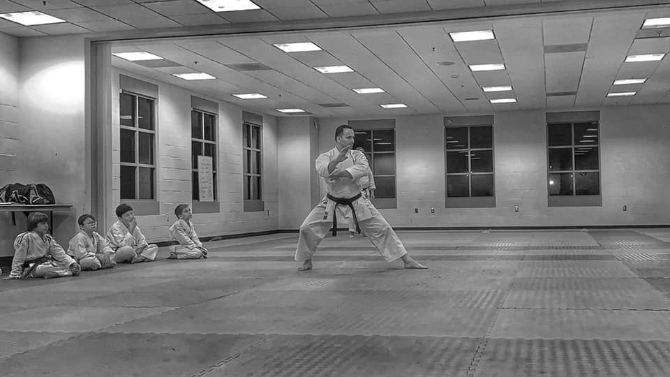 A black and white photo of a man practicing karate in a gym.