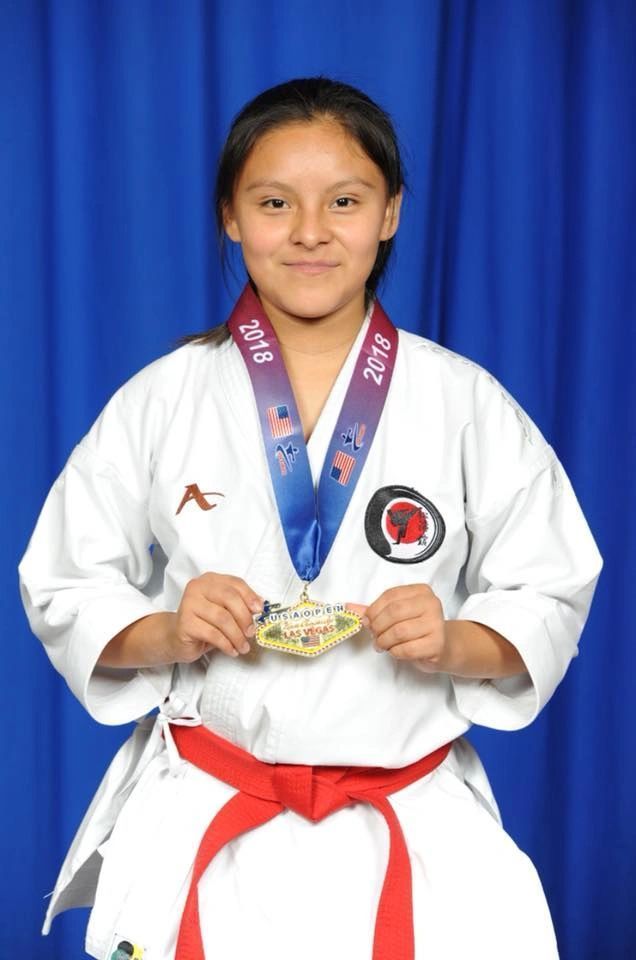A girl in a karate uniform is holding a medal around her neck.