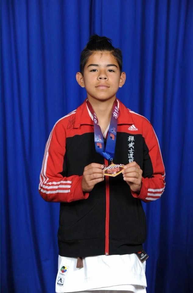 A young boy wearing a medal around his neck is standing in front of a blue curtain
