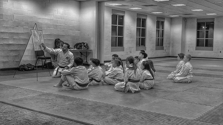 A group of children are sitting on the floor in a karate class.