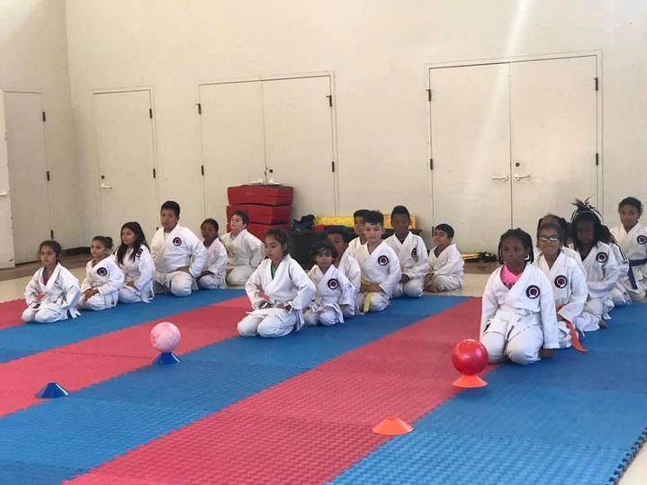 A group of children are sitting on a mat in a gym.