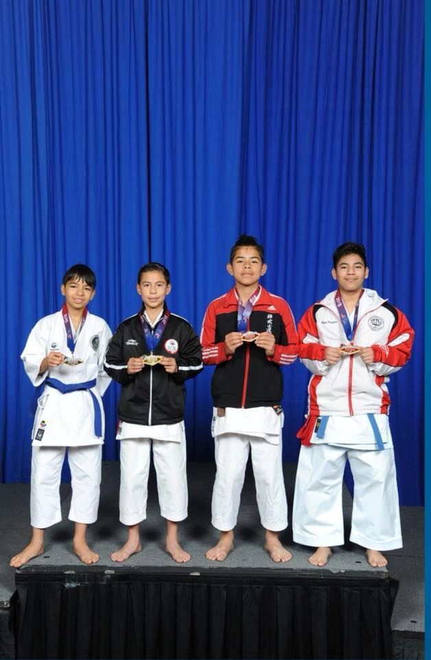 A group of young men in karate uniforms are standing on a stage holding medals.