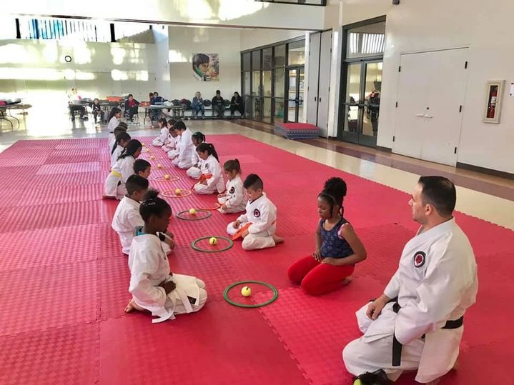A group of children are sitting on a red mat in a gym.