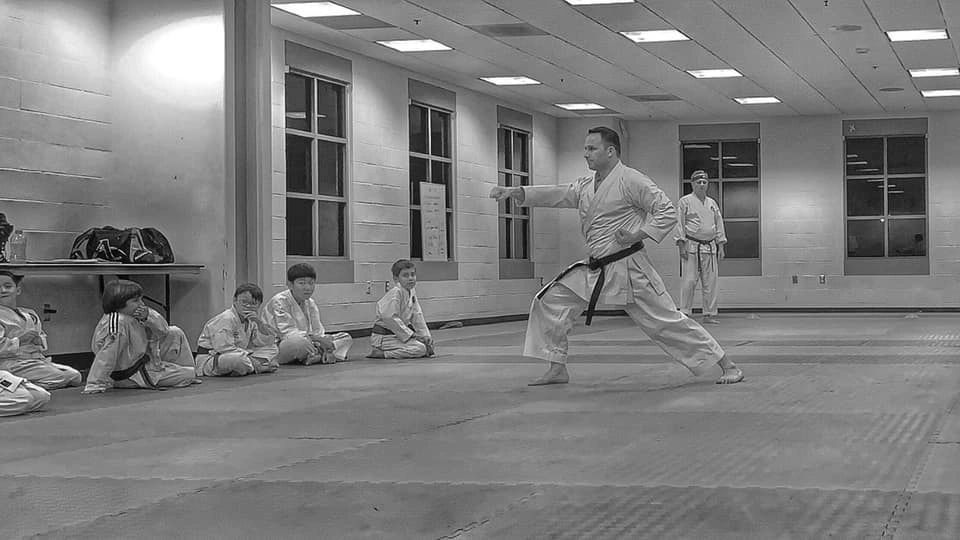 A black and white photo of a group of people practicing martial arts in a gym.