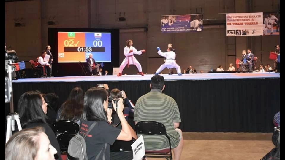 A group of people watching a karate match with a scoreboard that says 02 00