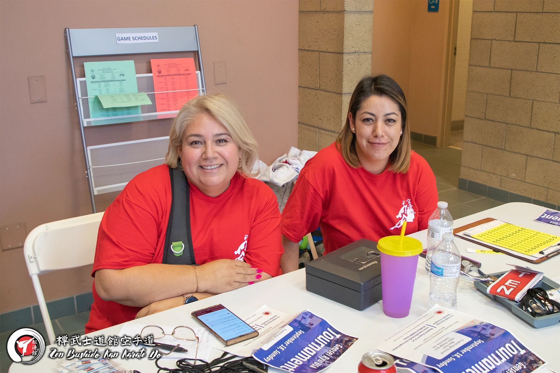 Two women in red shirts are sitting at a table.