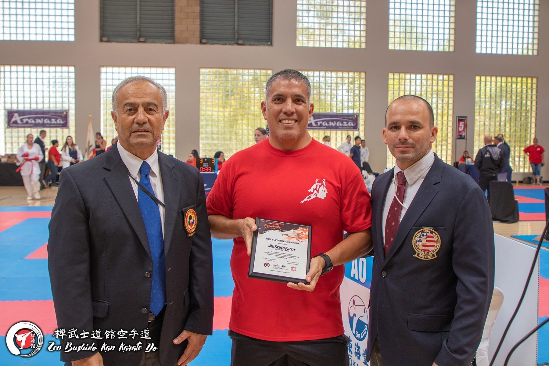 A man in a red shirt is holding a certificate while standing next to two men in suits.