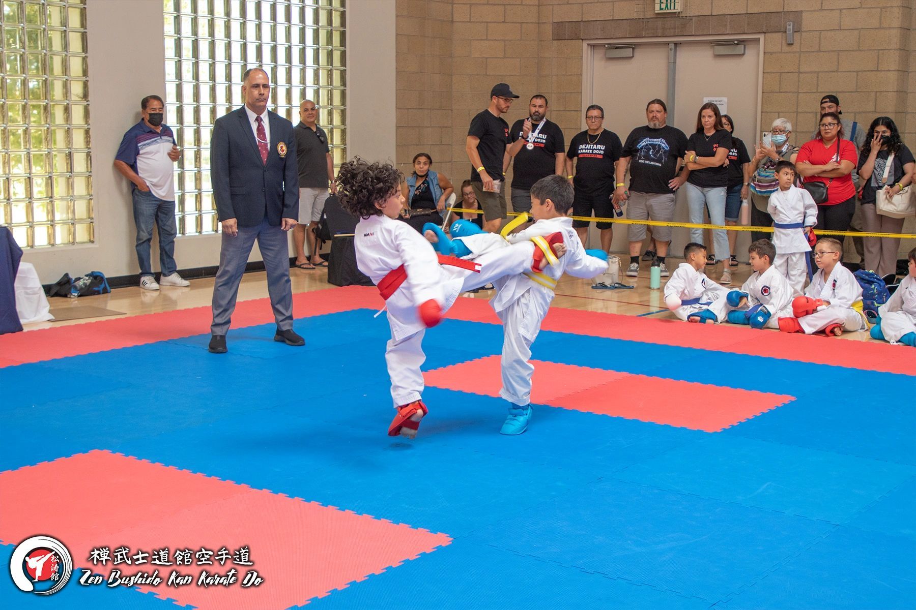 A group of children are playing karate on a mat in a gym.