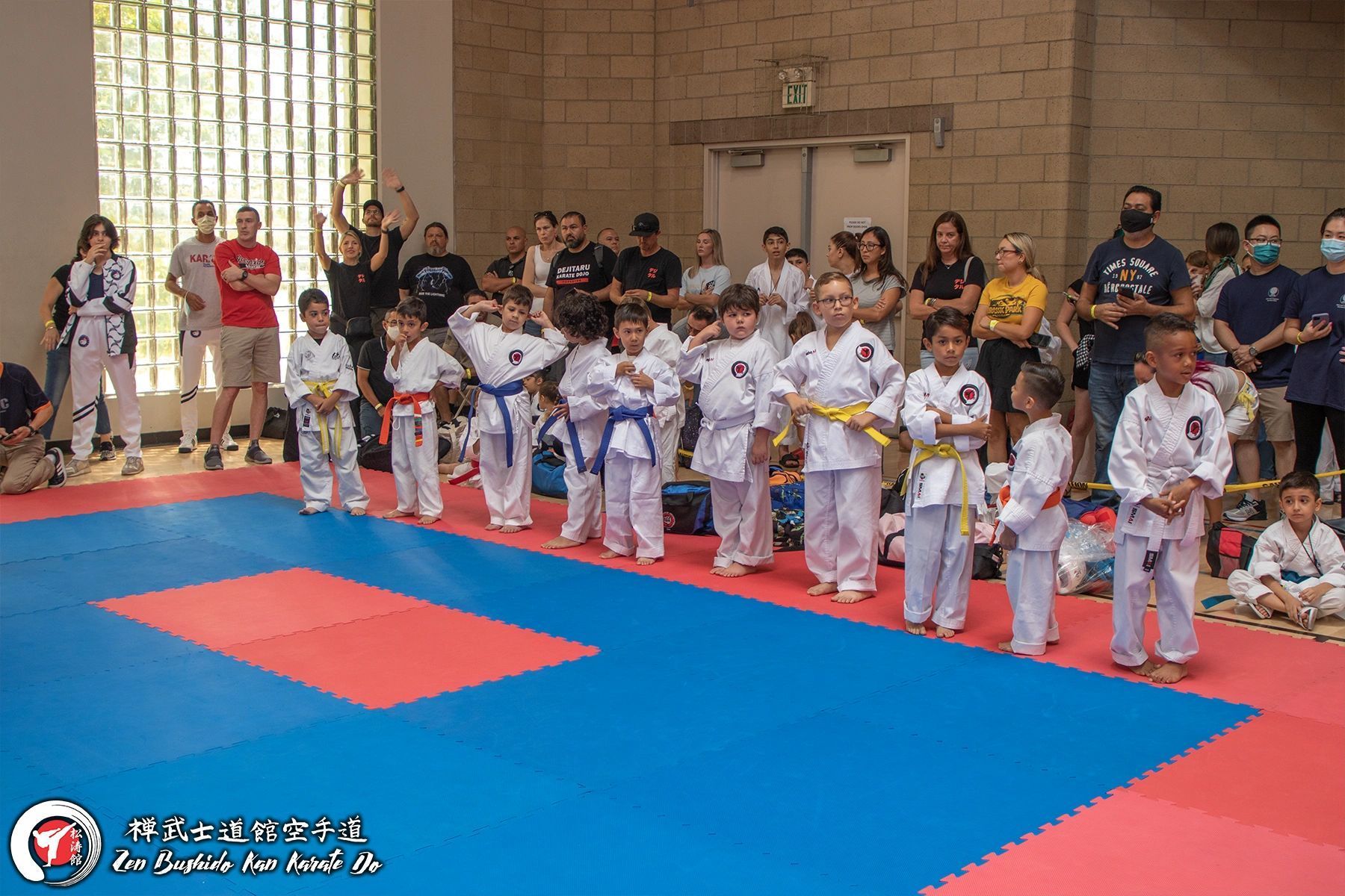 A group of children in karate uniforms are standing on a mat in a gym.