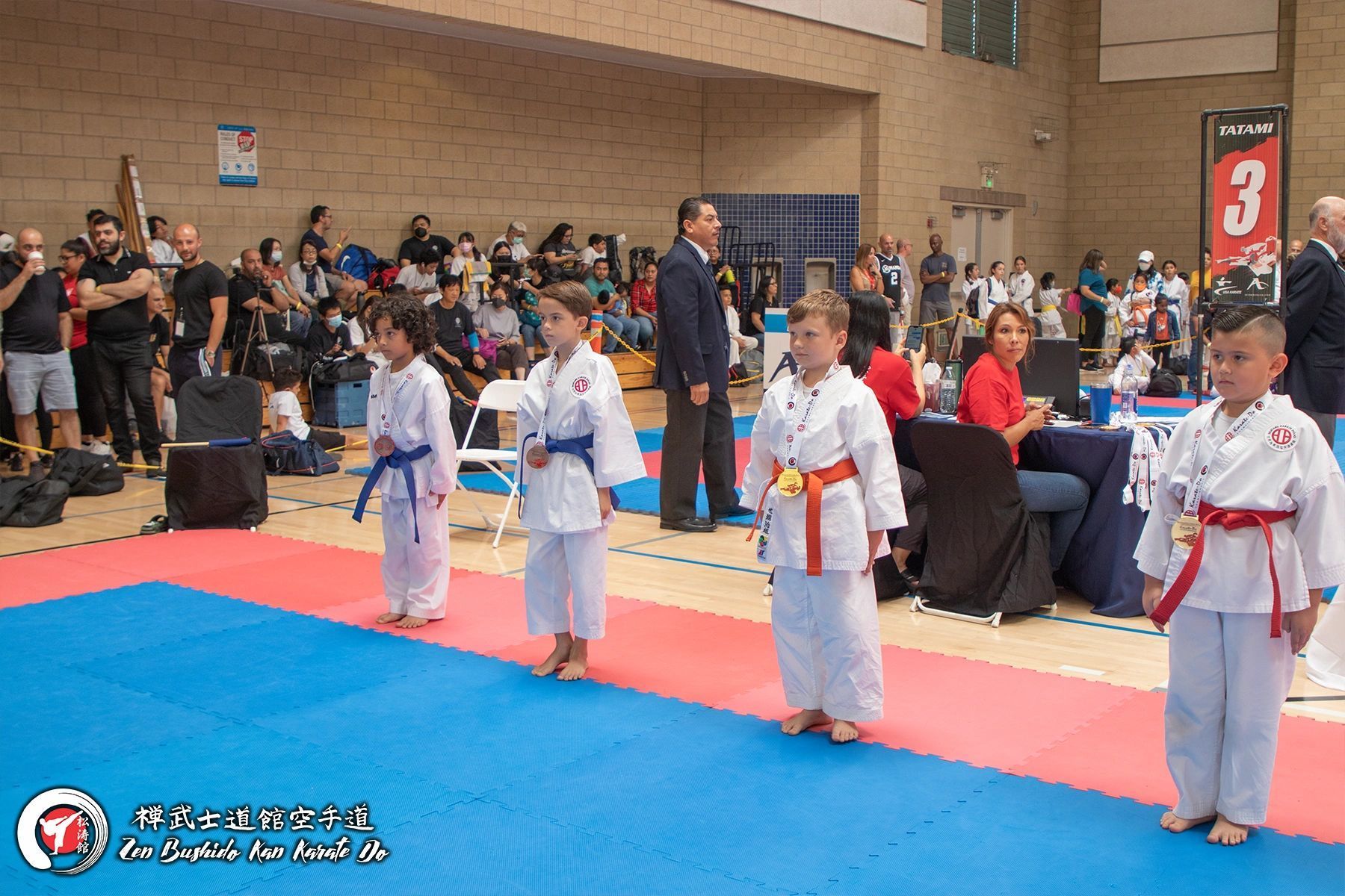 A group of young boys in karate uniforms are standing on a mat in a gym.