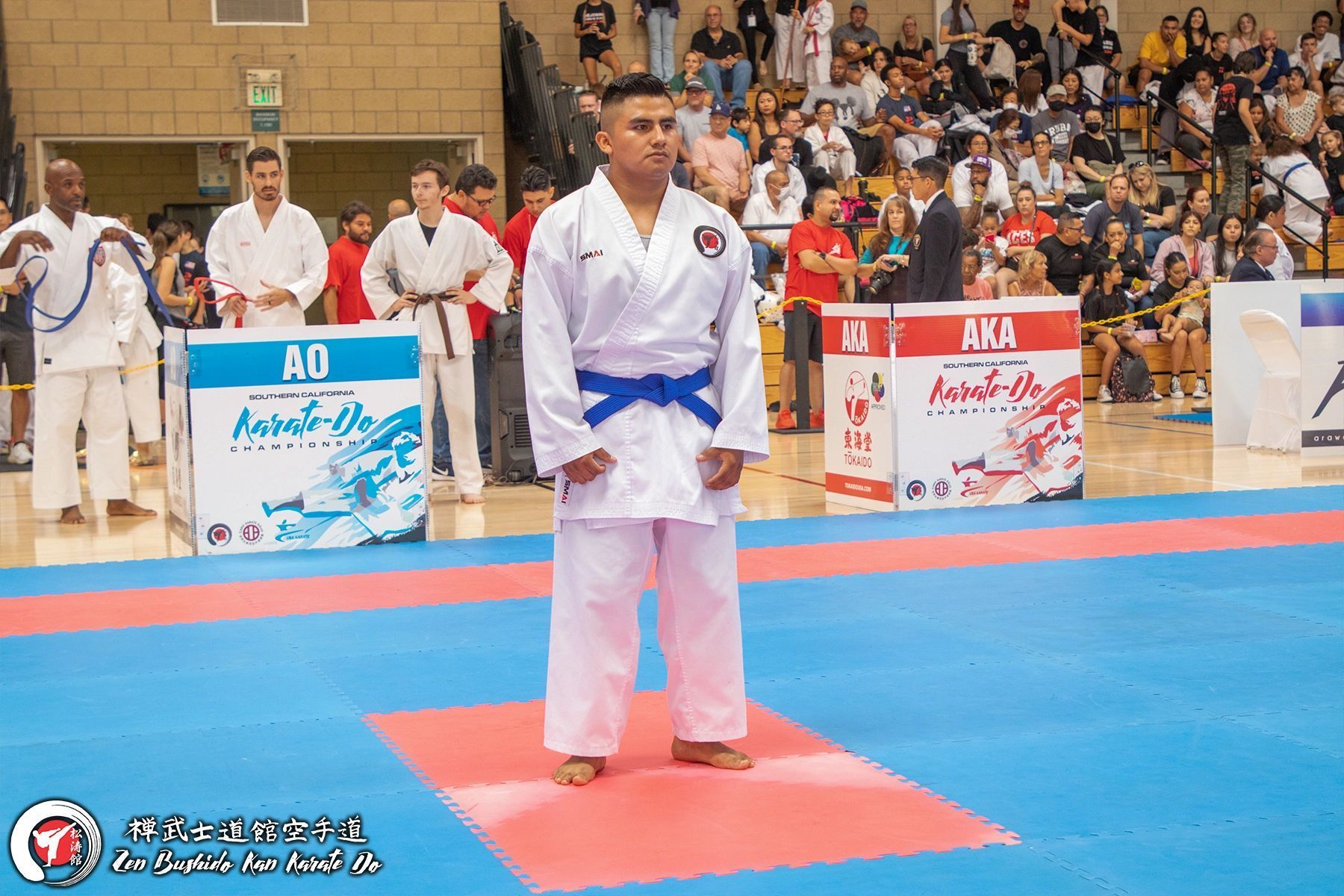 A man in a karate uniform is standing on a mat in front of a crowd.