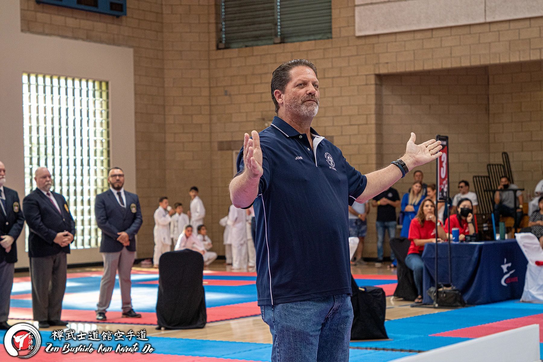 A man in a blue shirt is standing in a gym with his arms outstretched.