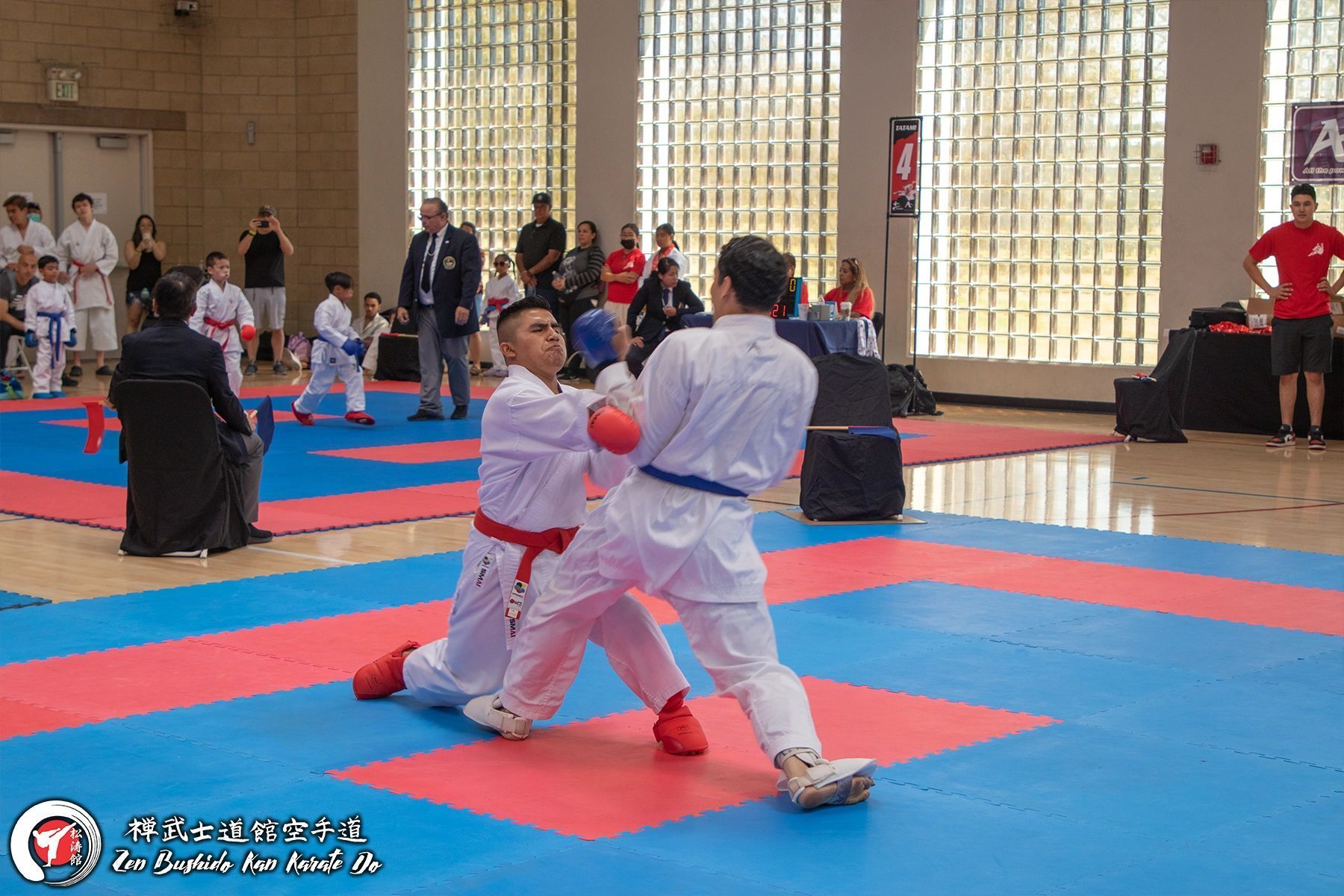 Two karate fighters are fighting on a mat in a gym.