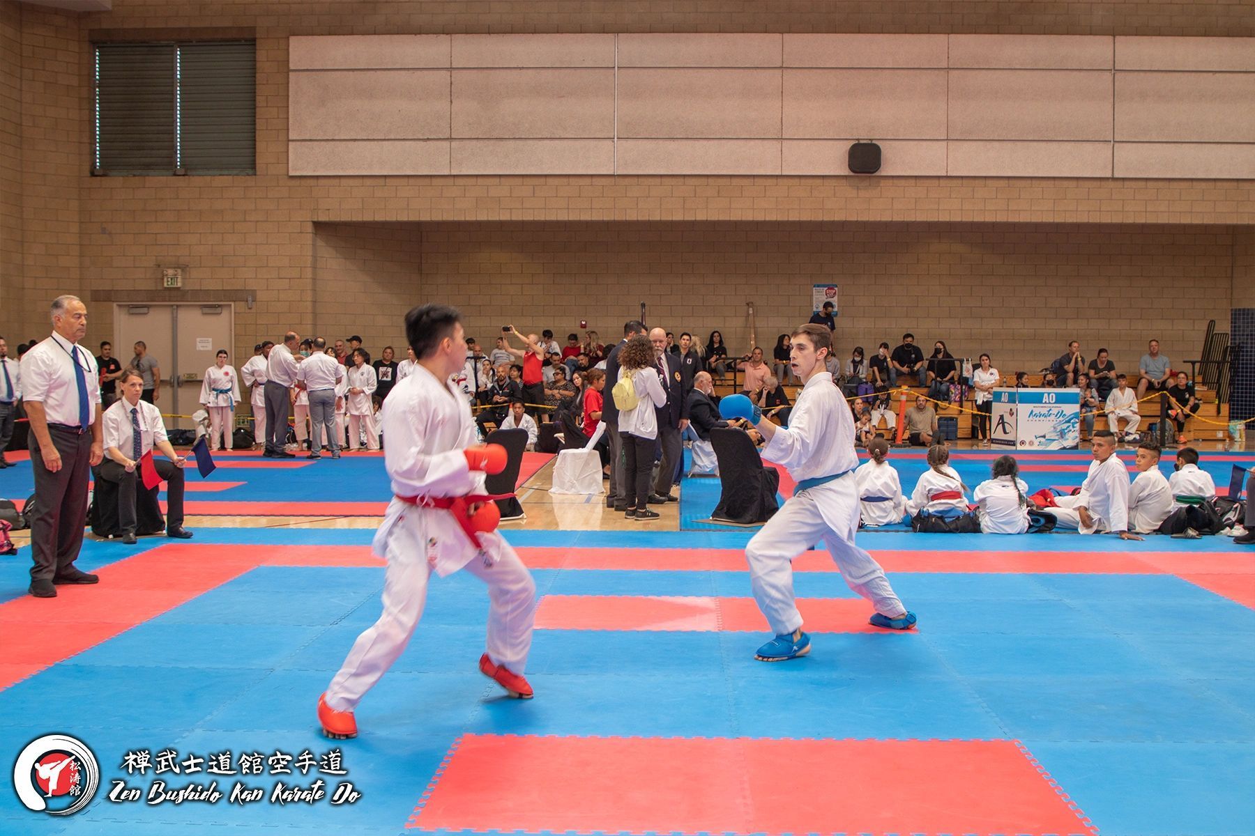 Two karate fighters are fighting on a mat in a gym.