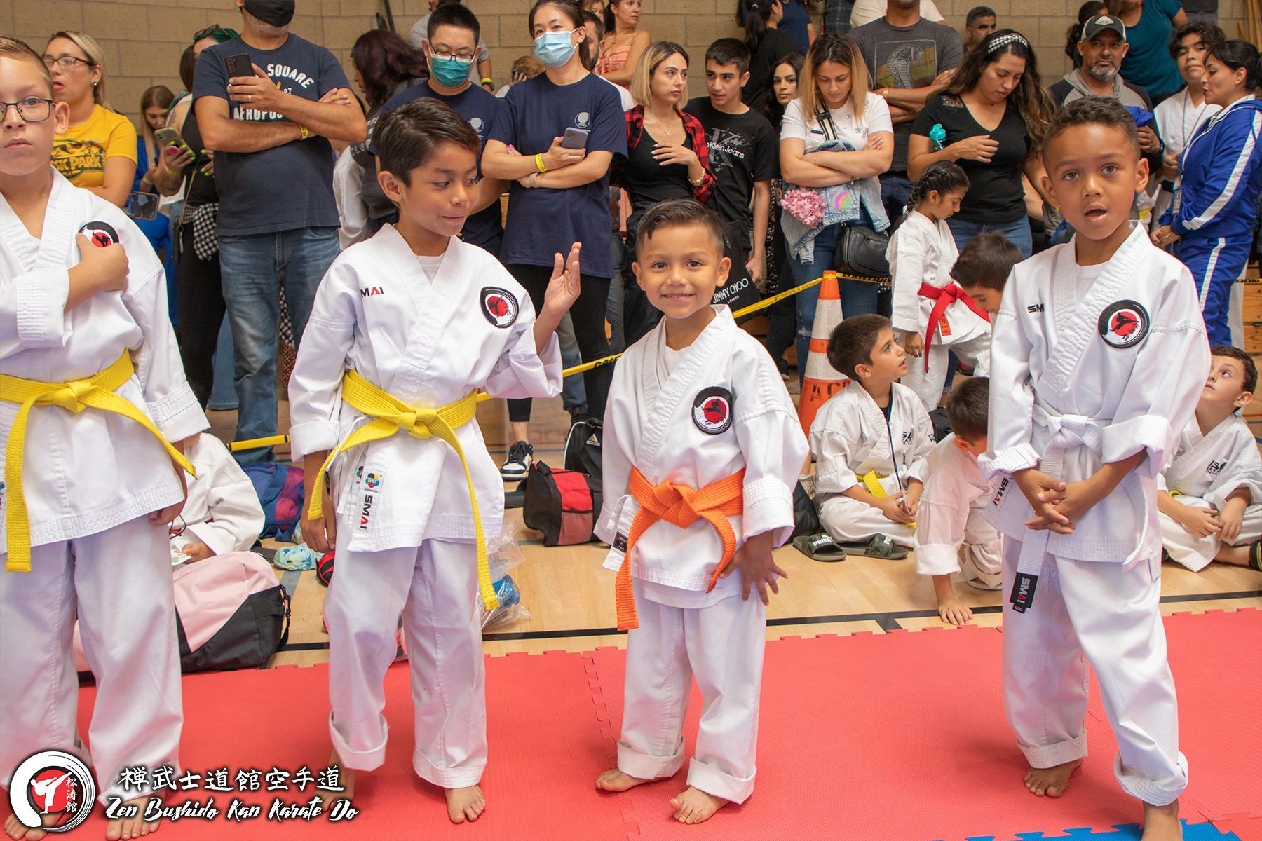 A group of young children in karate uniforms are standing on a mat in front of a crowd.